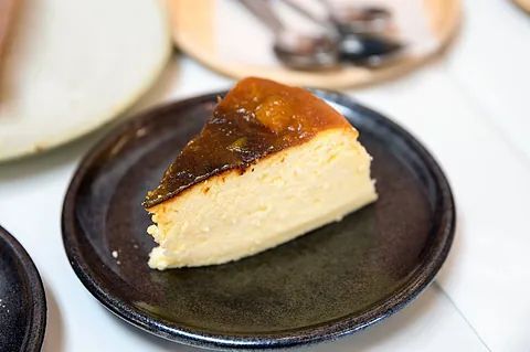 Una rebanada de tarta de queso está en un plato negro.