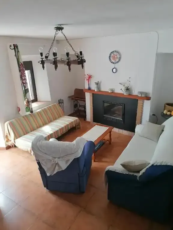 Sala de estar con chimenea, sofás, sillón, mesa de centro de madera, lámpara de araña y ventana.