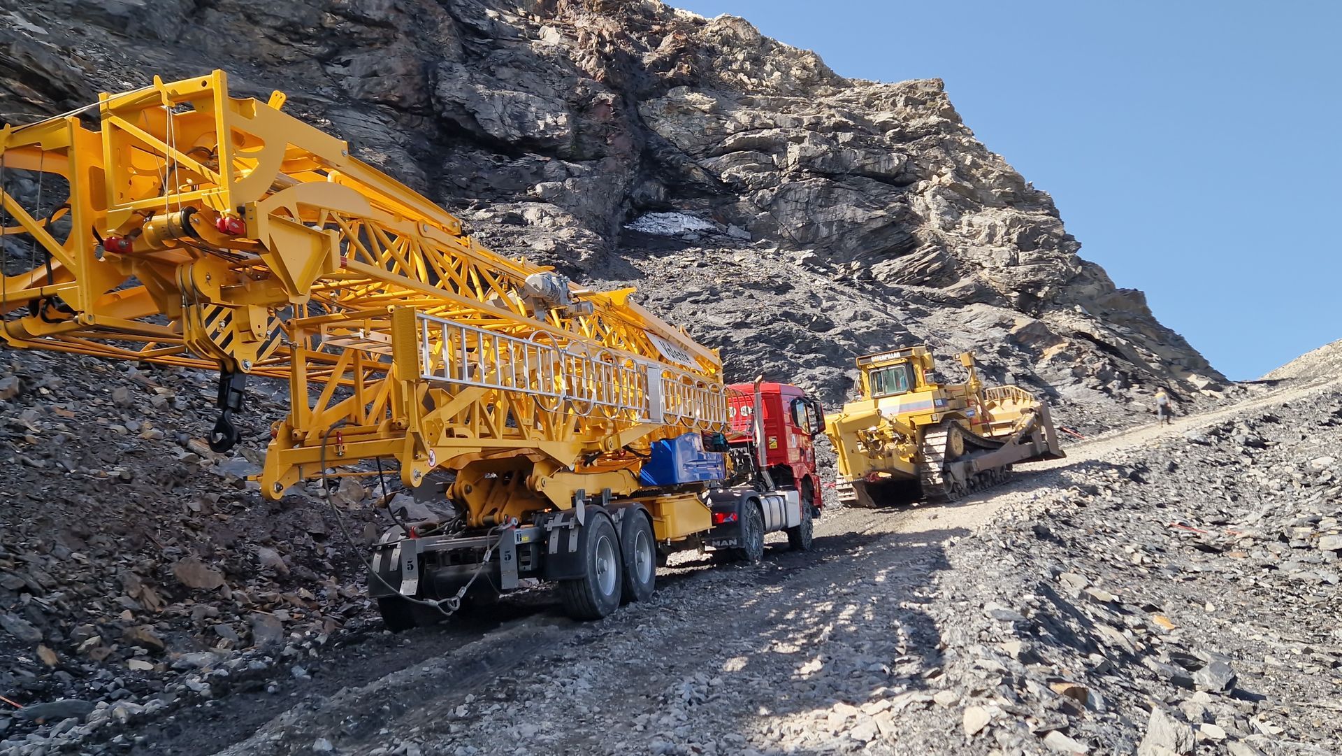 Une grue jaune sur un camion gravit une pente rocheuse.