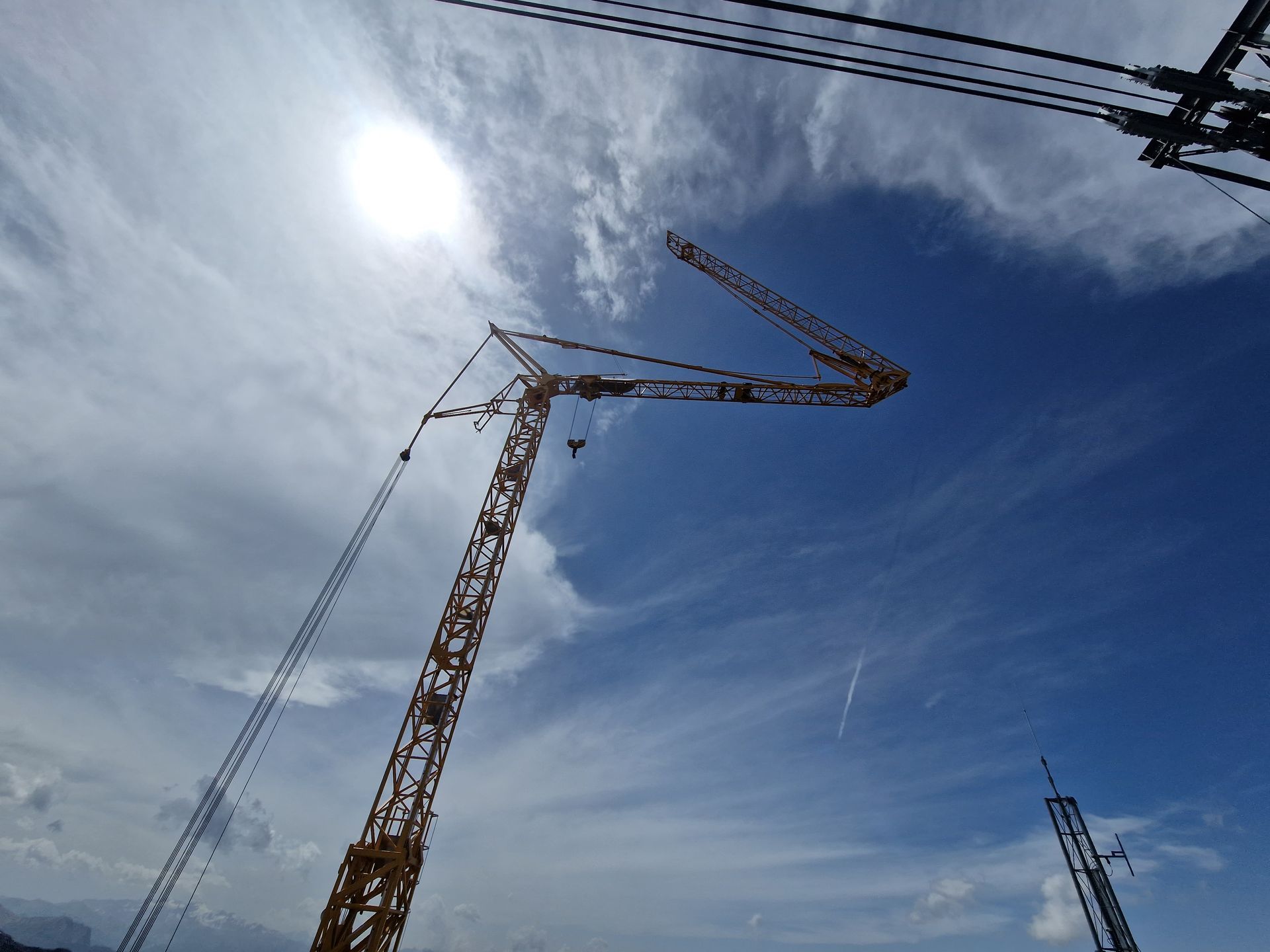 Grue de chantier jaune sur un ciel bleu nuageux, soleil partiellement masqué.