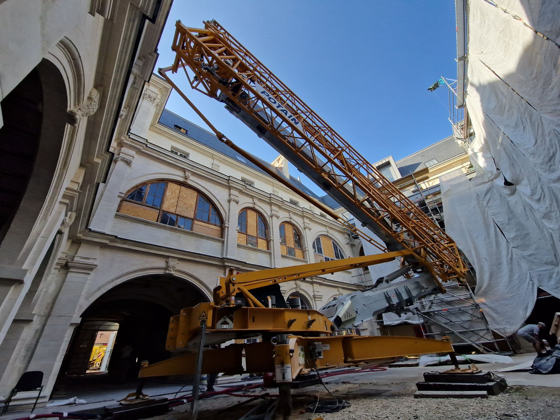 Une grue jaune se dresse devant un bâtiment. Le bras de la grue est déployé au-dessus du bâtiment.
