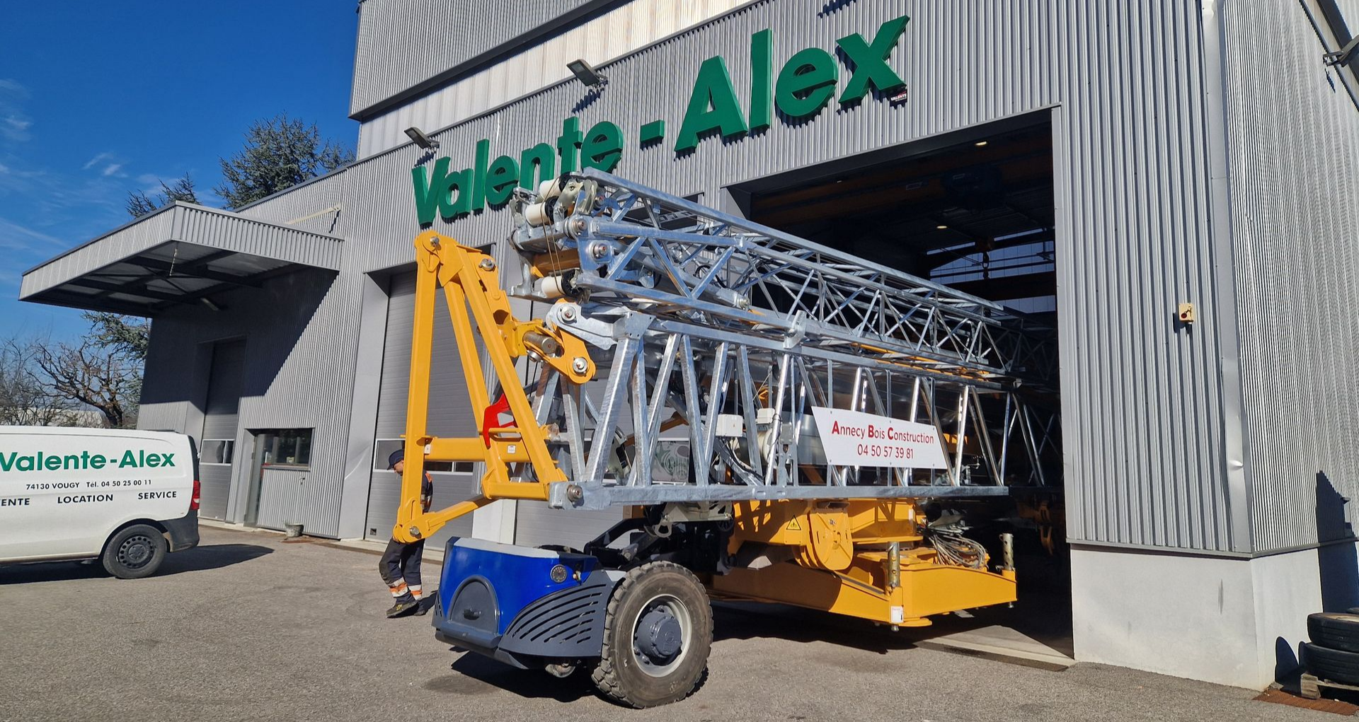 Une grue à châssis argenté sort de l'entrepôt d'Alex Grues.