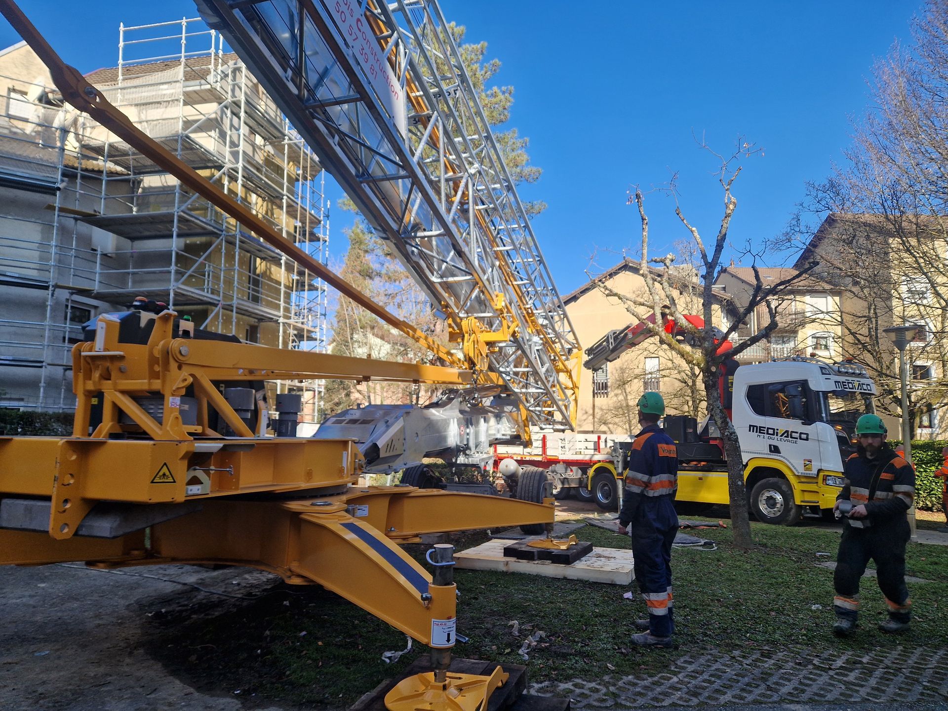 Une grue de chantier en cours d'assemblage près d'un bâtiment entouré d'échafaudages.