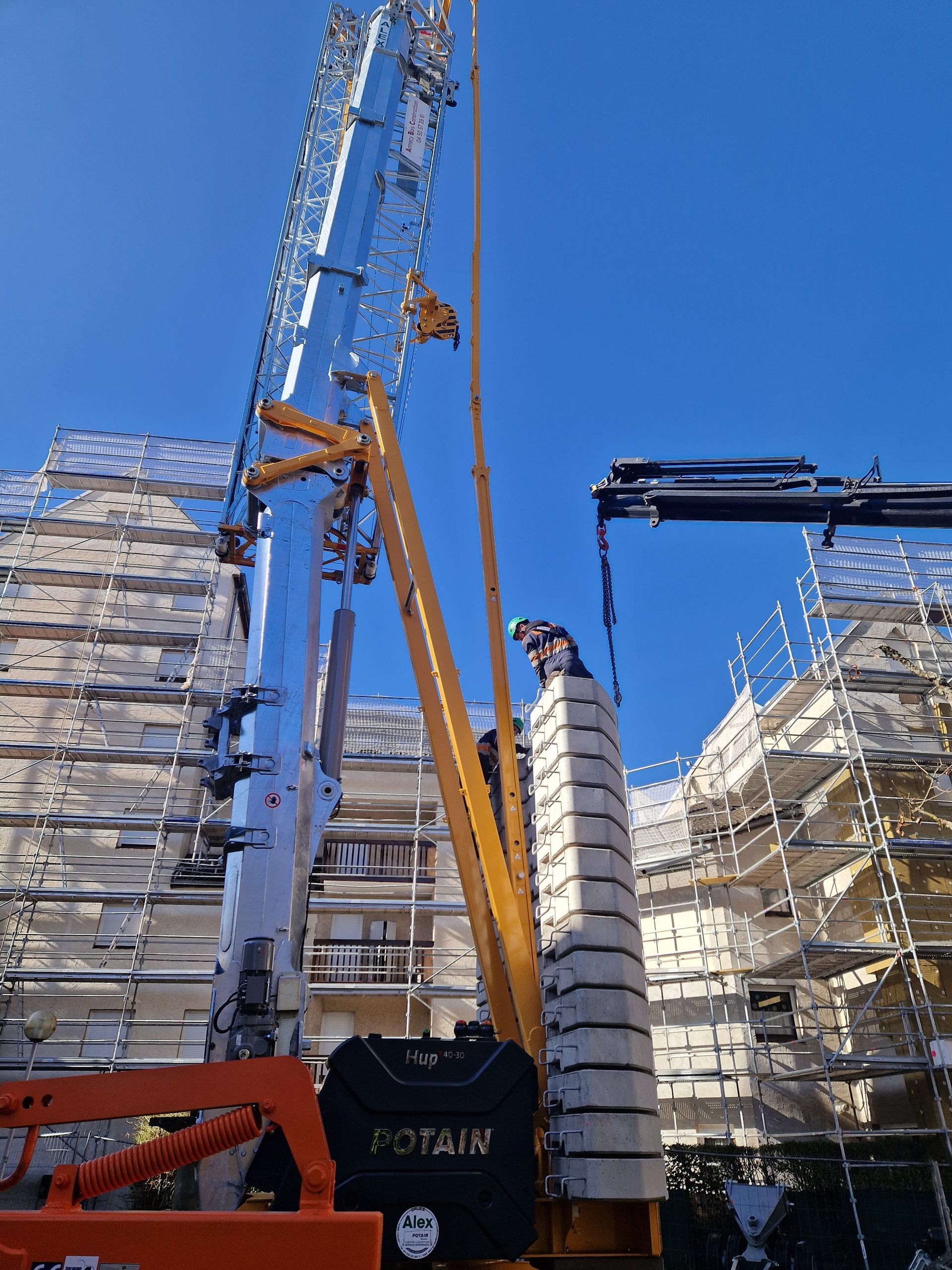 Grue de chantier soulevant des matériaux sur un chantier avec échafaudages.