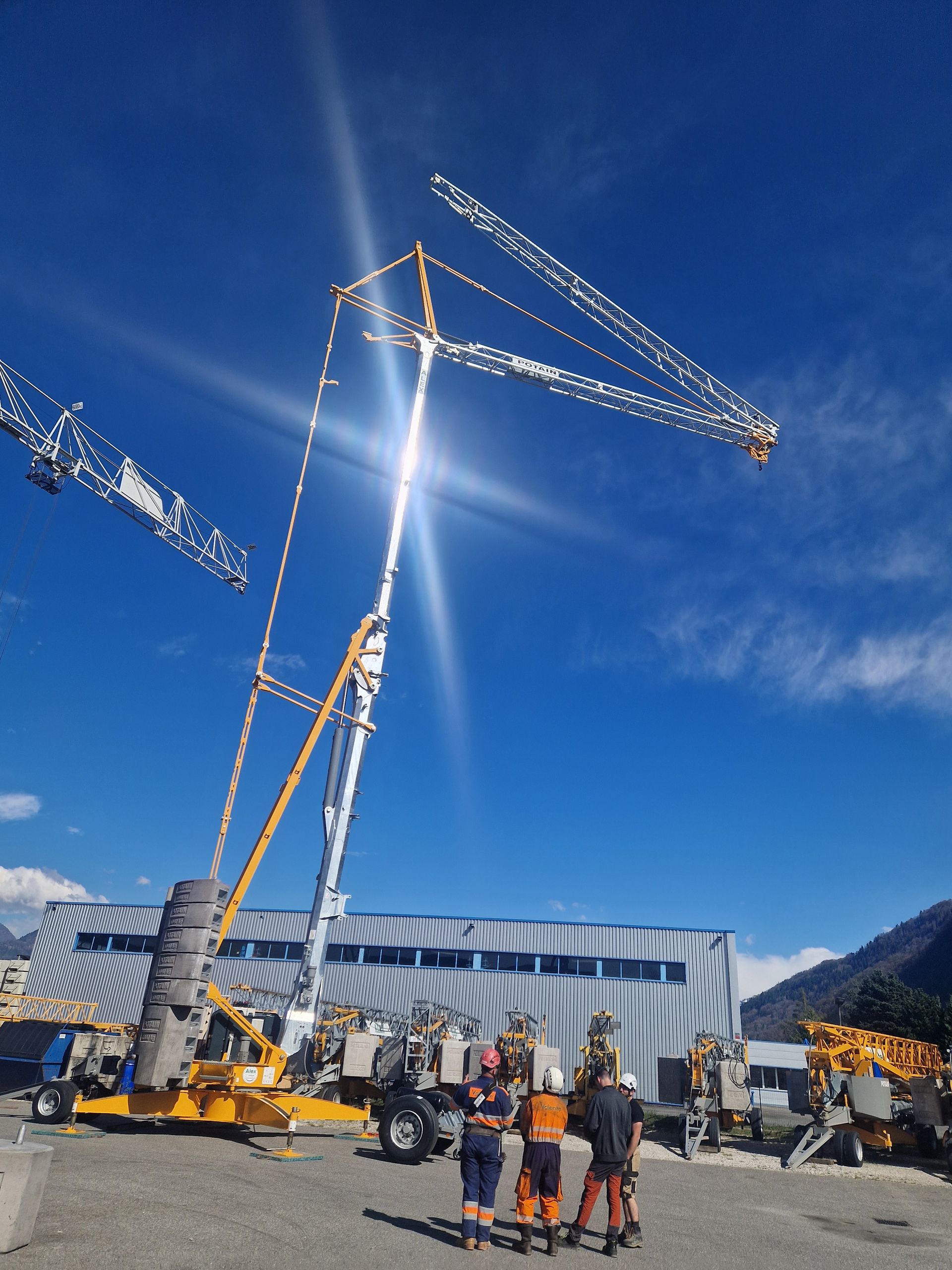 Des ouvriers du bâtiment se tiennent près d'une grue argentée et jaune.