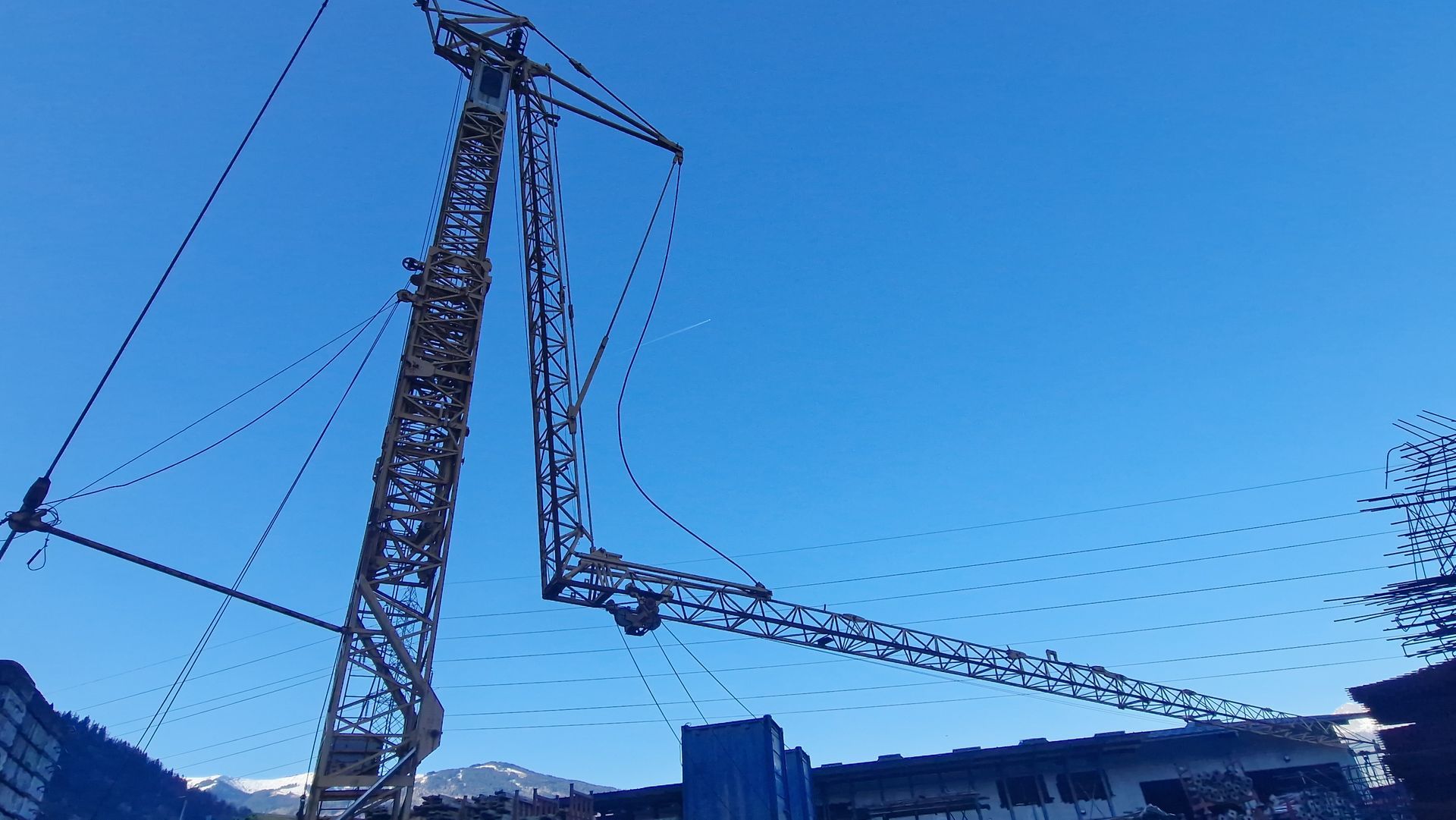 Une grande grue de chantier, ciel bleu et montagnes en arrière-plan.