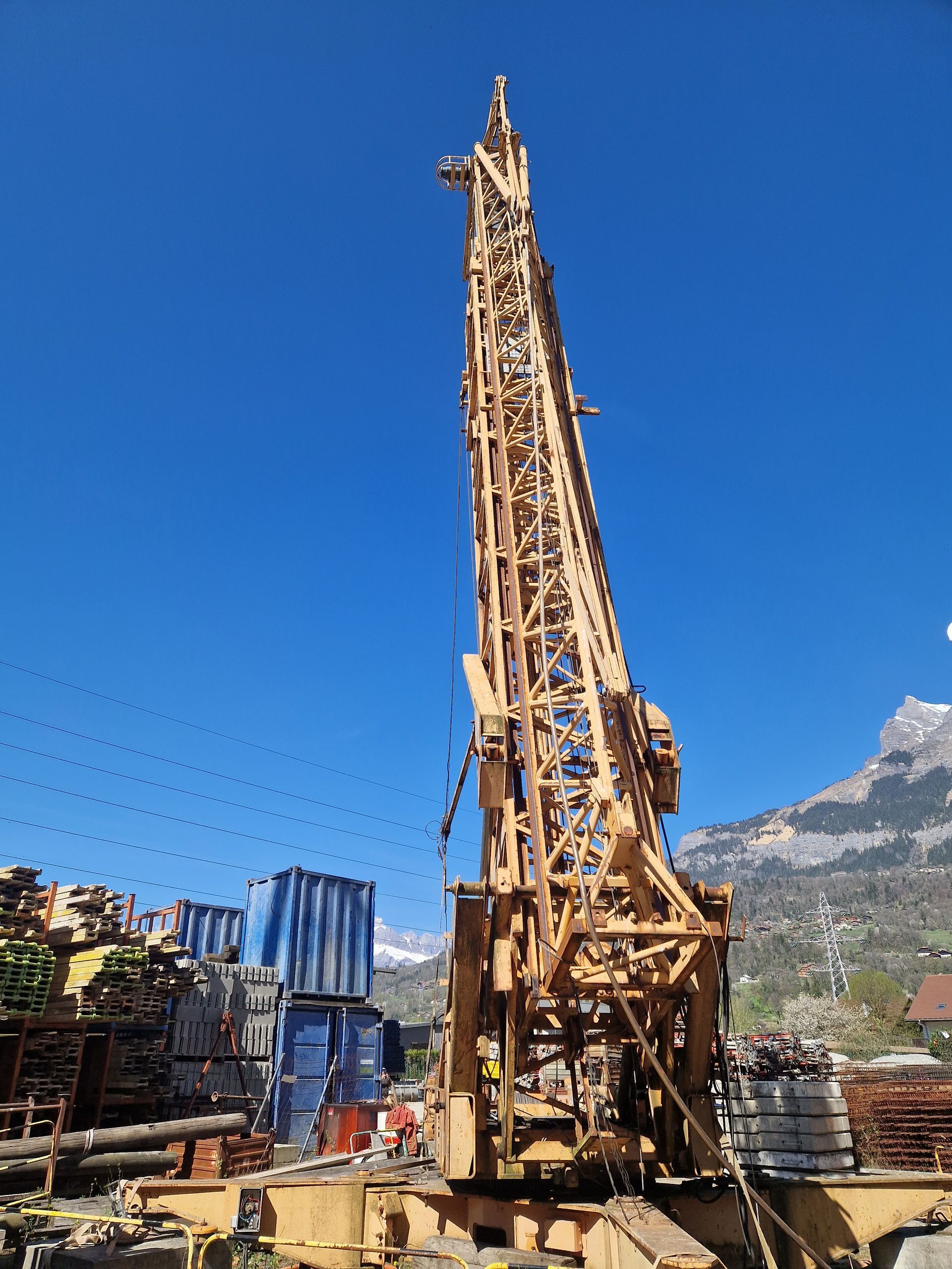 Plateforme de forage jaune sur fond de ciel bleu, montagnes en arrière-plan.