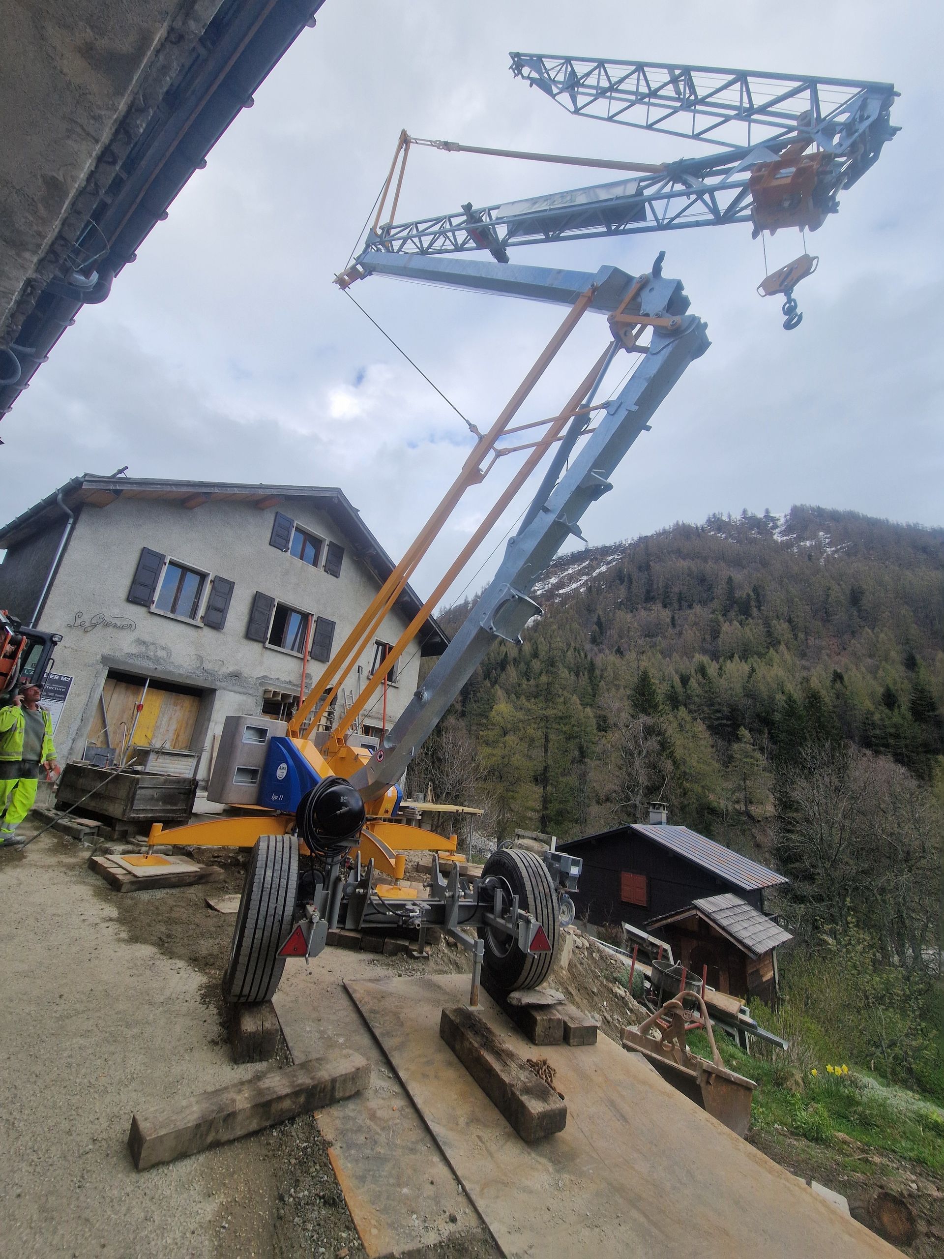 Une grue bleue et jaune en construction ou en réparation près d'un bâtiment rural.