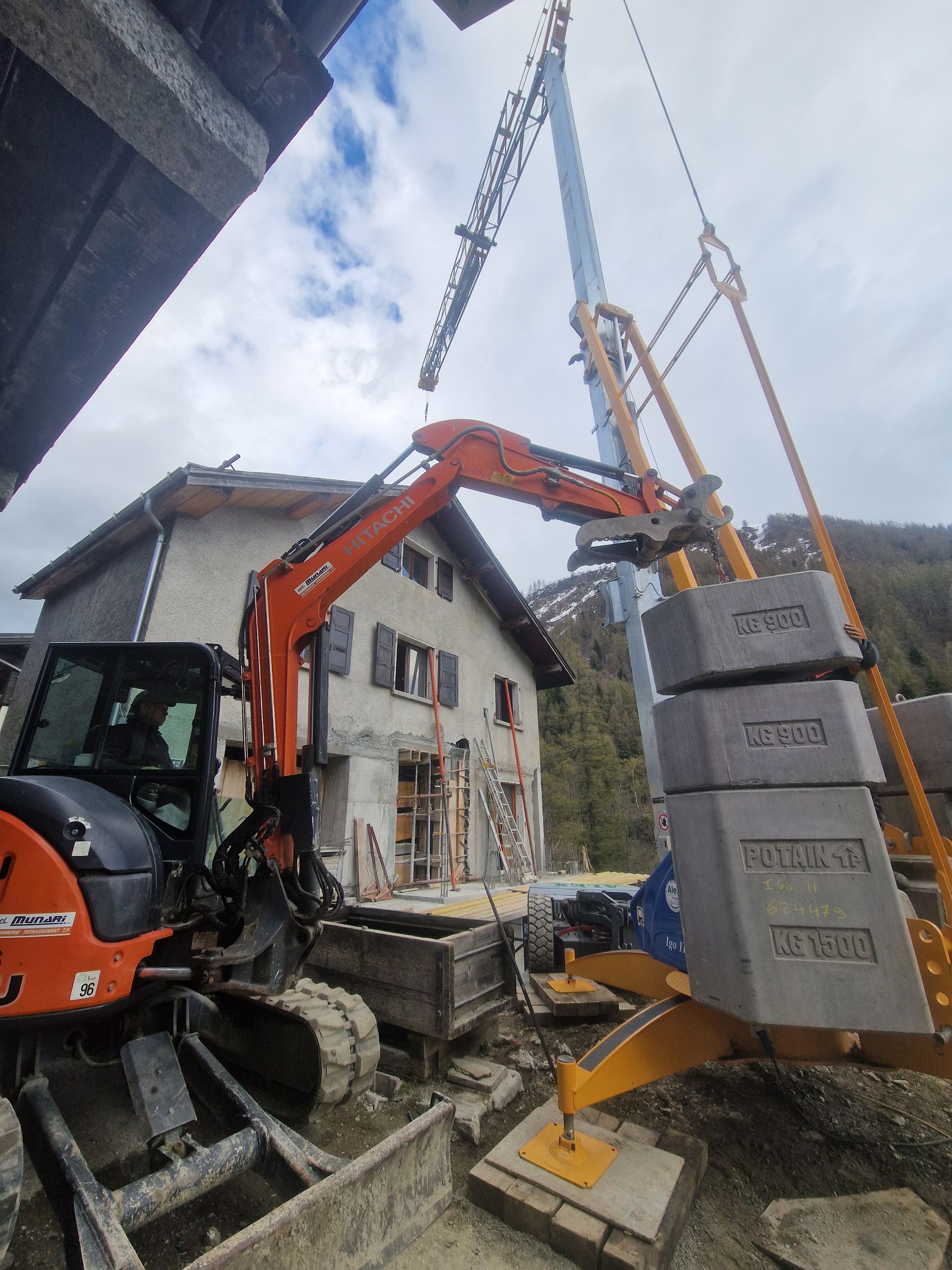 Une excavatrice et une grue soulèvent des blocs de béton près d'un bâtiment en construction.