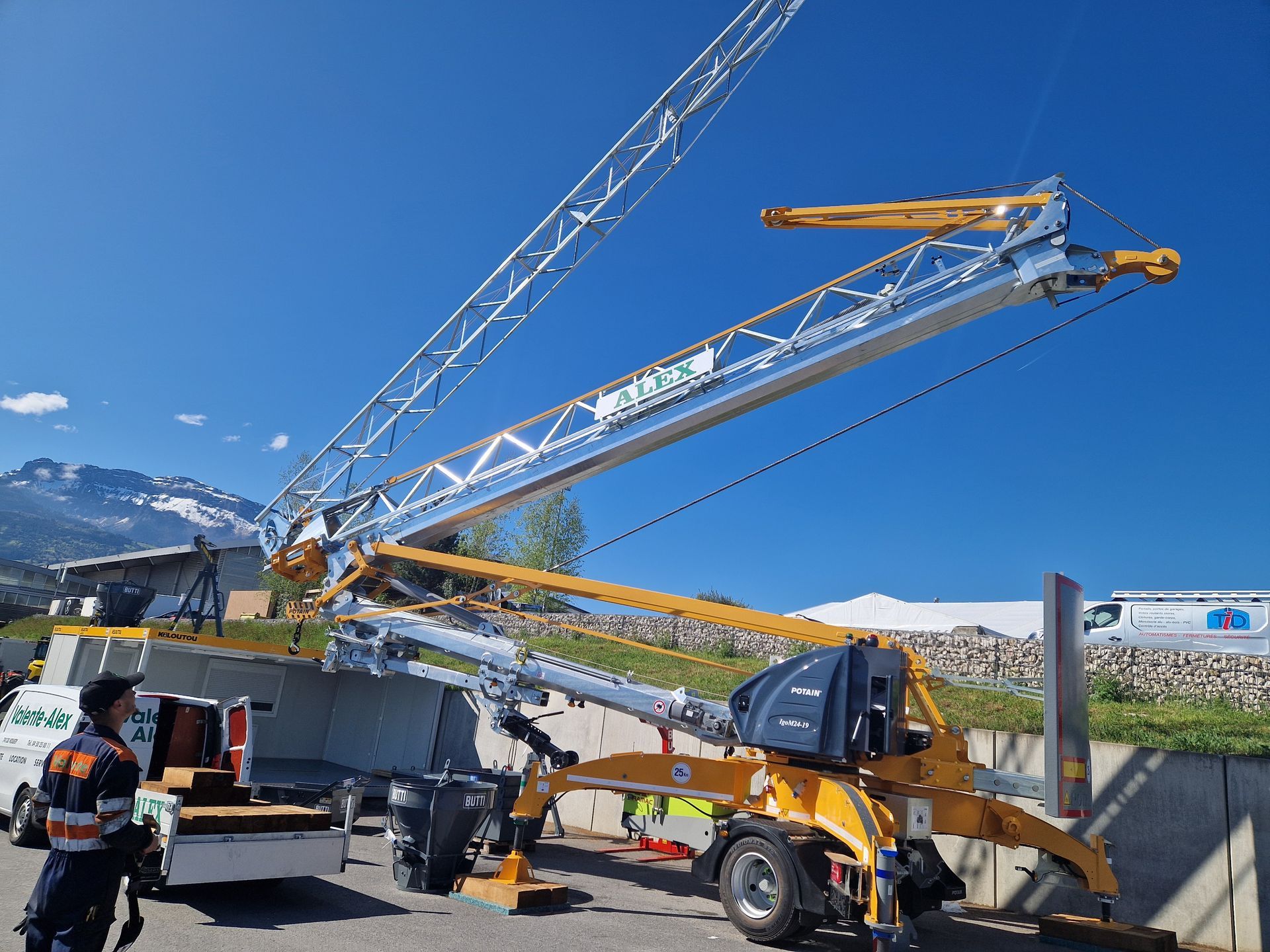 Grue de chantier jaune déployée, avec un ouvrier devant, en extérieur.