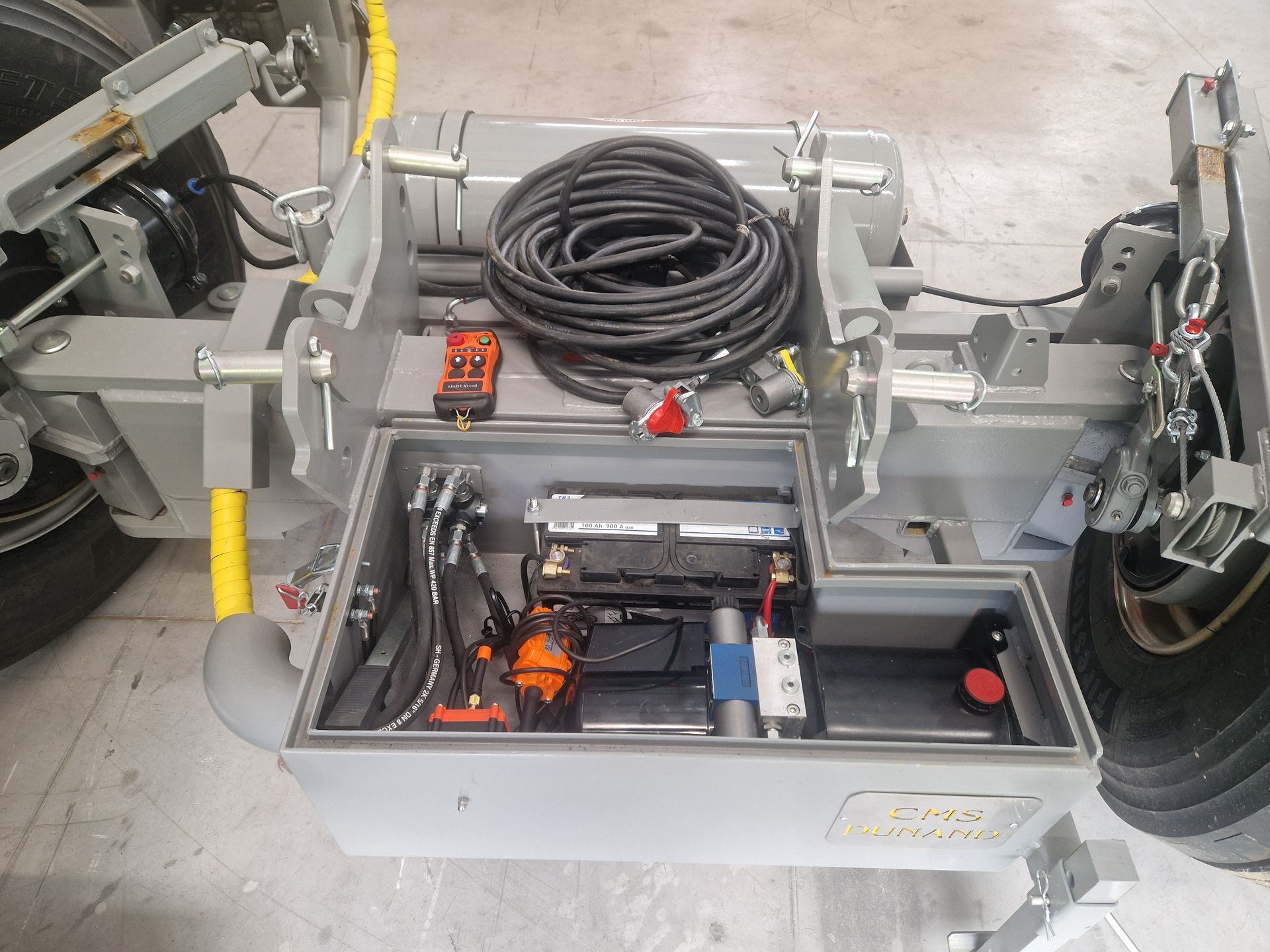 Machine grise avec un câble enroulé noir, des outils et un compartiment ouvert avec des composants internes.