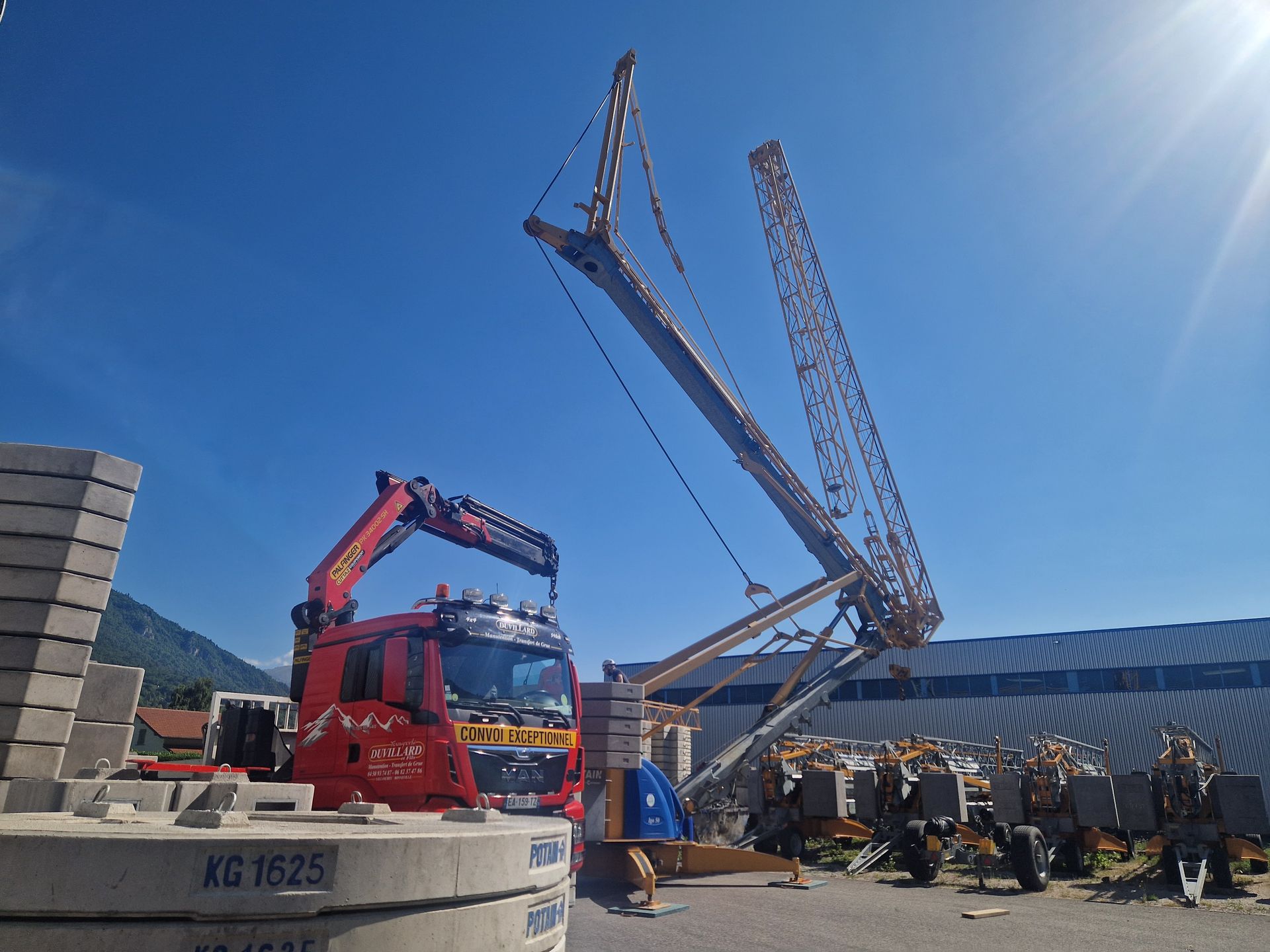 Camion rouge avec bras de grue à côté d'une grue jaune inclinée.