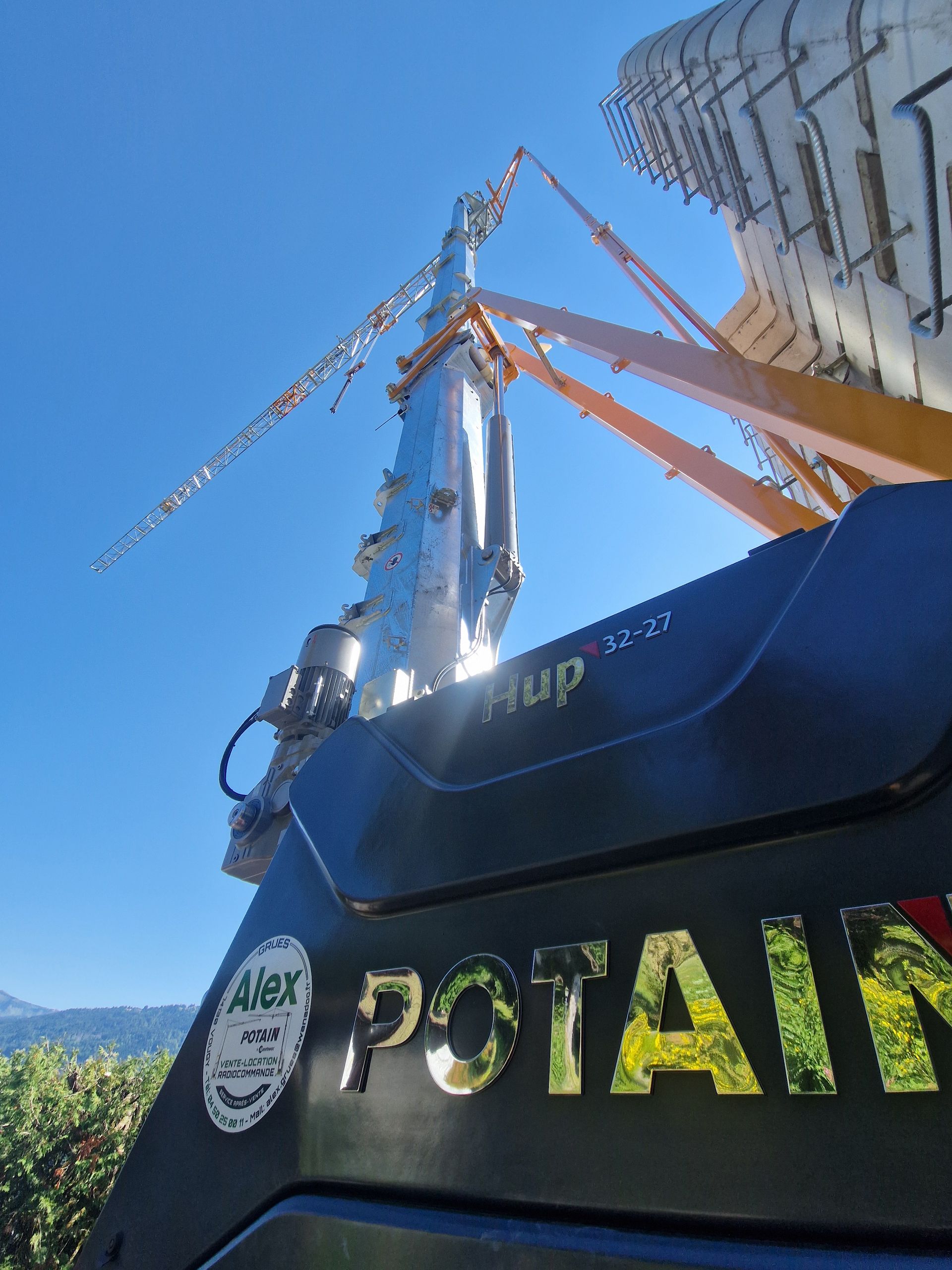 Une grue Potain s'étend vers une structure métallique sur fond de ciel bleu.