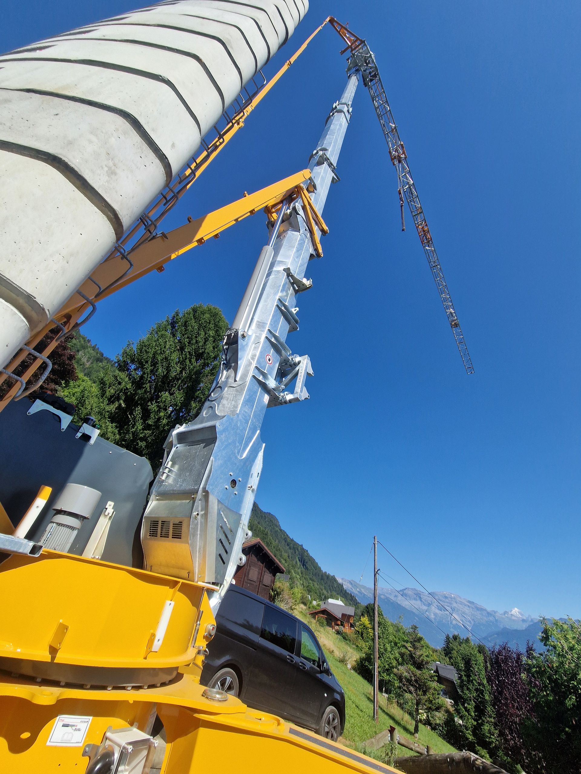 Un camion-pompe à béton déploie une flèche métallique vers une grande structure en béton.
