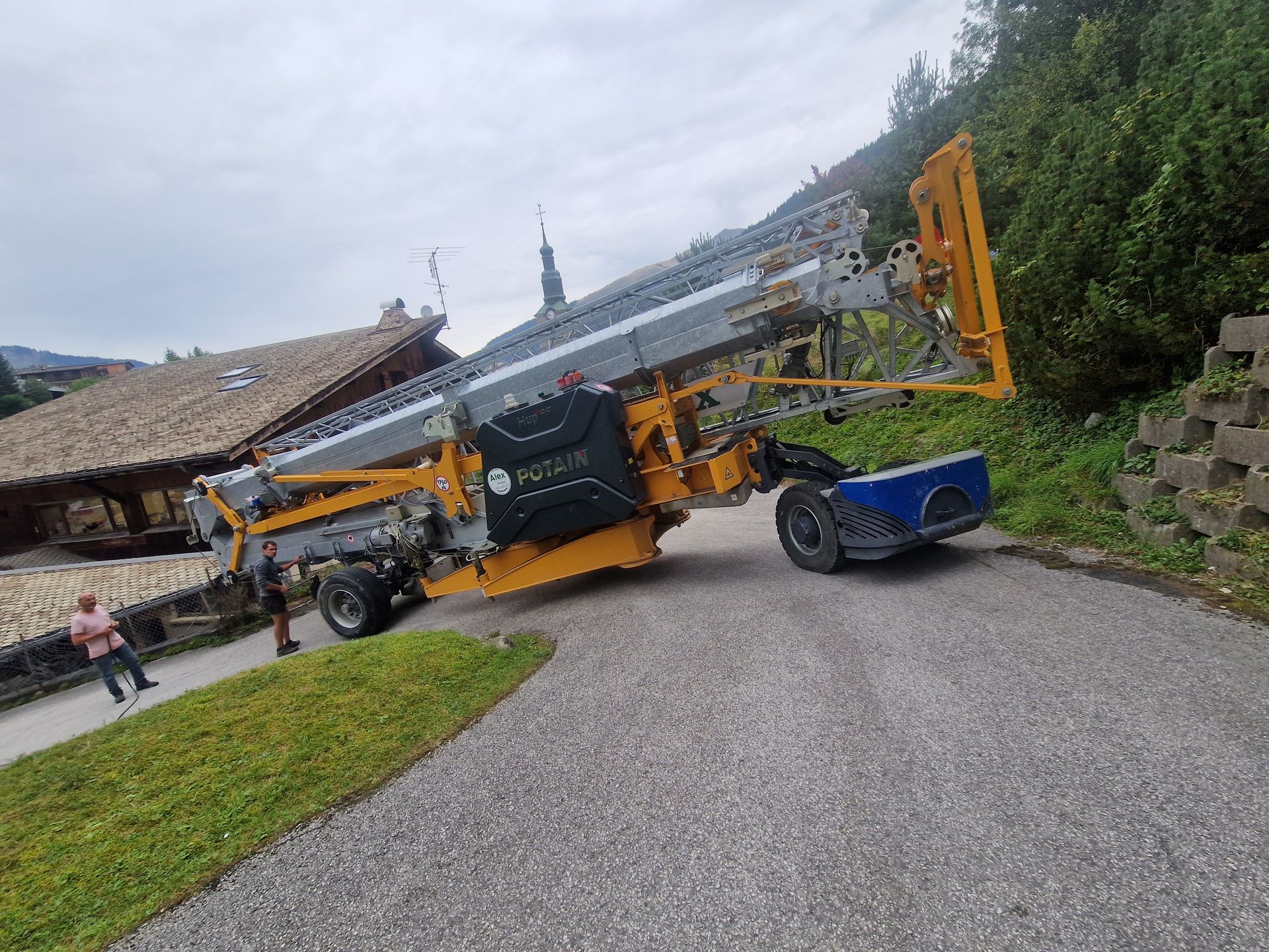 Un gros engin de chantier jaune et gris sur un chemin de gravier, près d'un bâtiment.