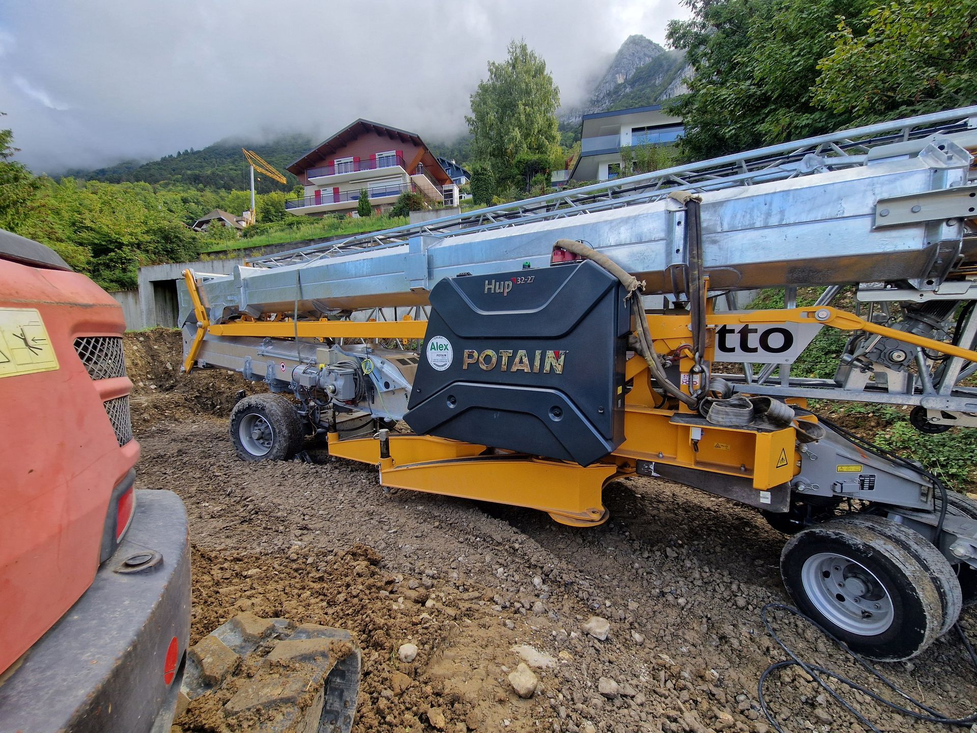 Grue de chantier de la marque Potain, pas encore montée, véhicule orange à gauche.