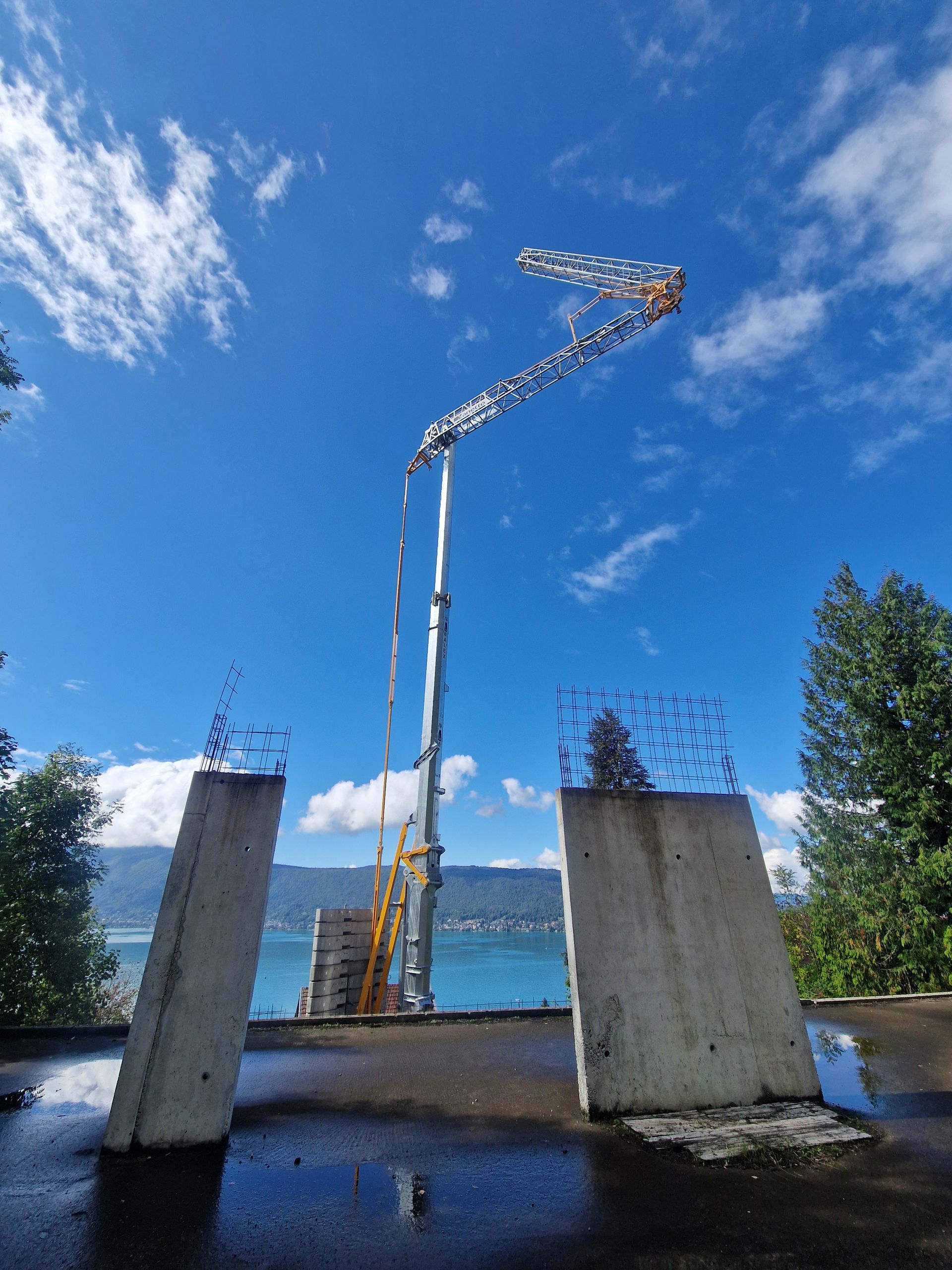 Chantier de construction avec une grue sur fond de ciel bleu. Murs en béton au premier plan et eau en arrière-plan.