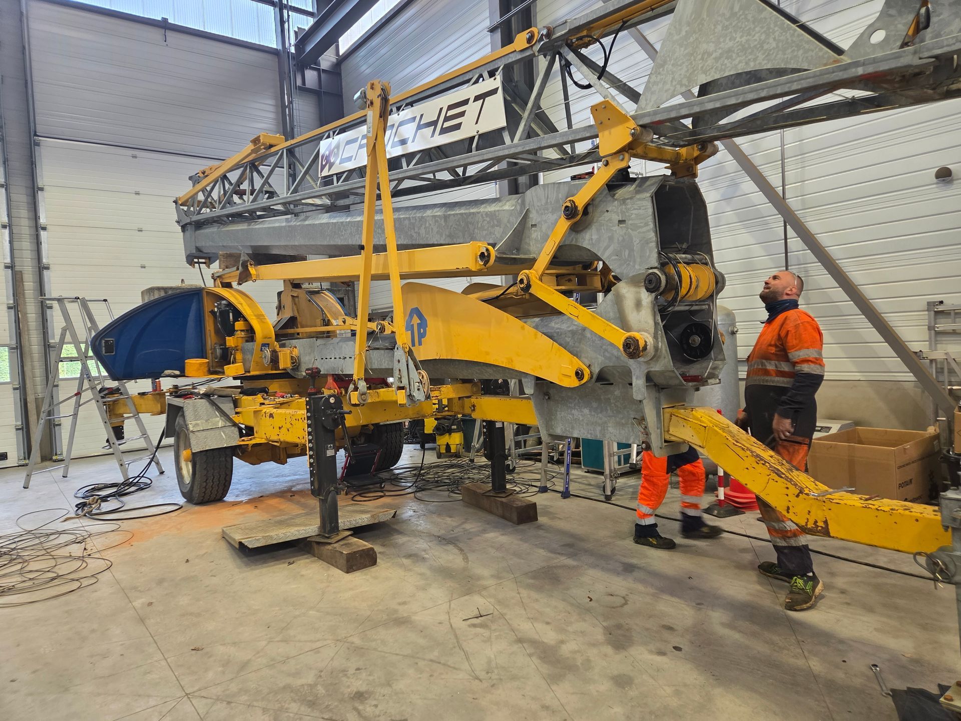 Une grande grue jaune et des ouvriers dans un atelier.