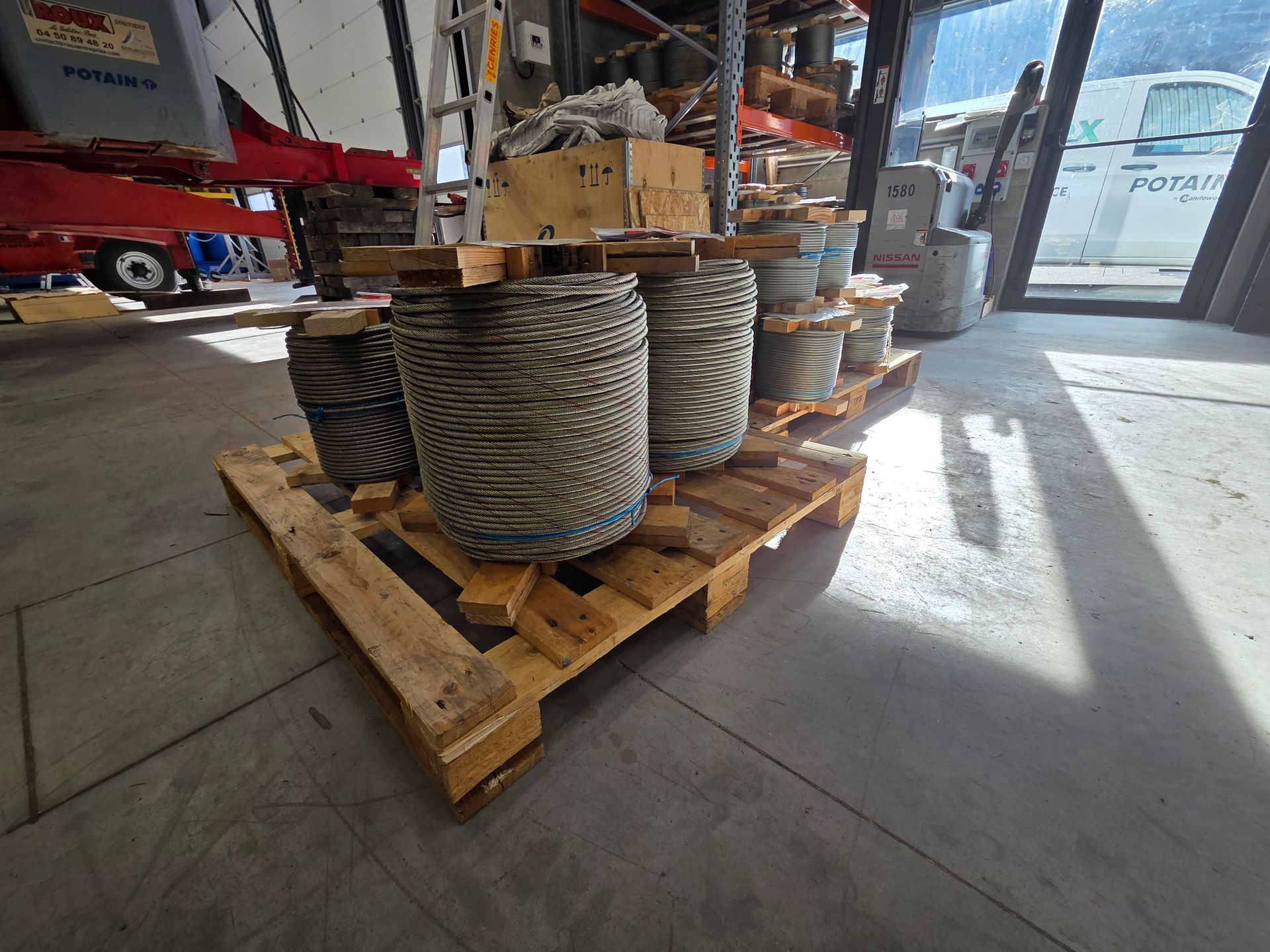 Palette en bois contenant plusieurs grandes bobines de corde dans un entrepôt.