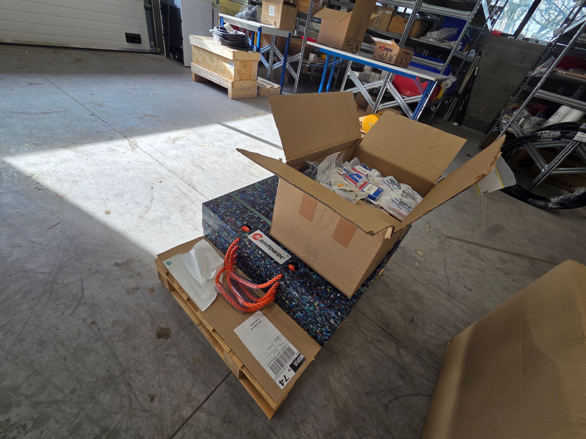 Boîte en carton ouverte sur une palette contenant des lunettes de sécurité et d'autres articles dans un entrepôt.