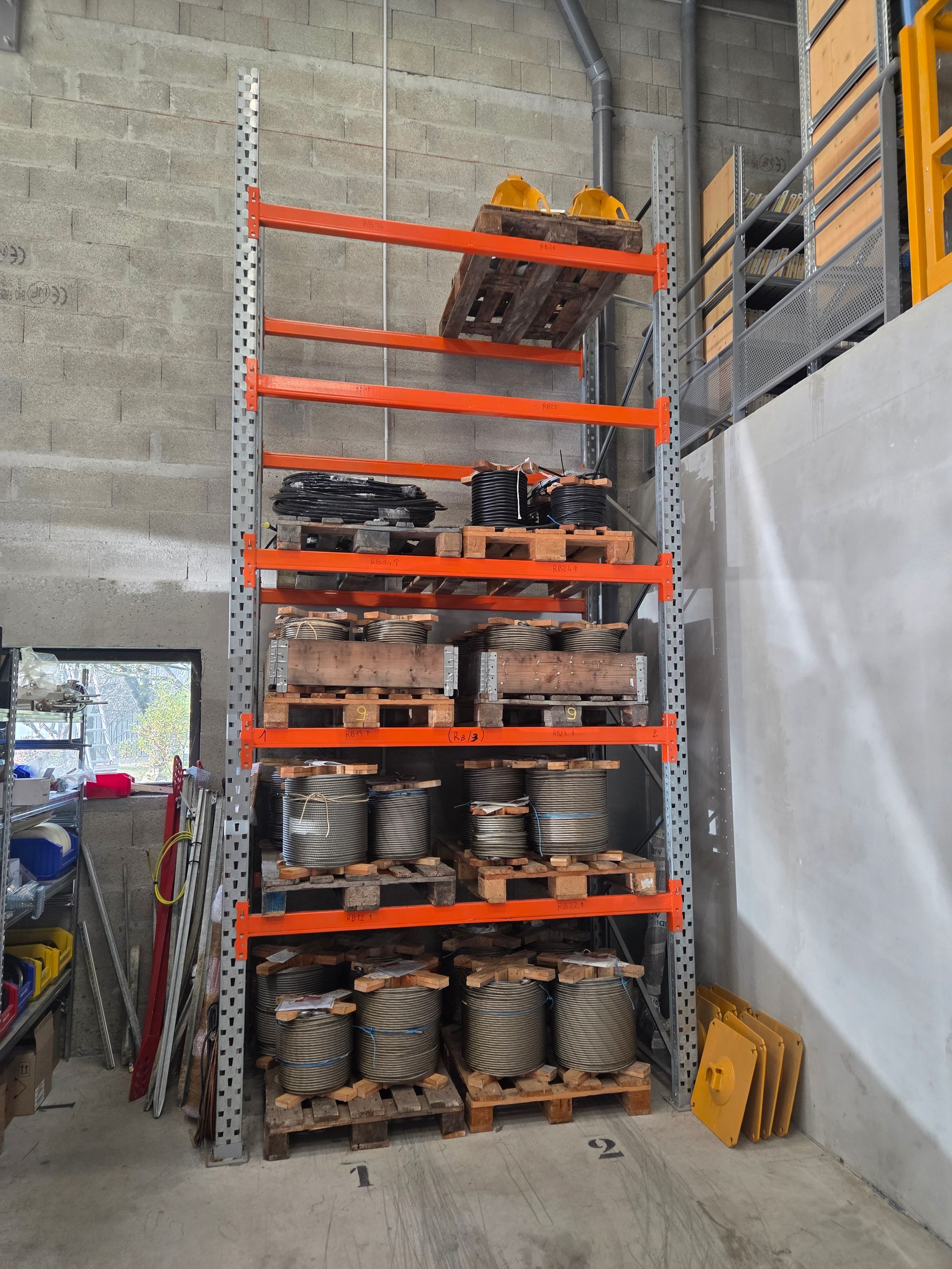 Étagère métallique remplie d'articles divers, notamment des palettes, des bobines de métal et des objets jaunes.