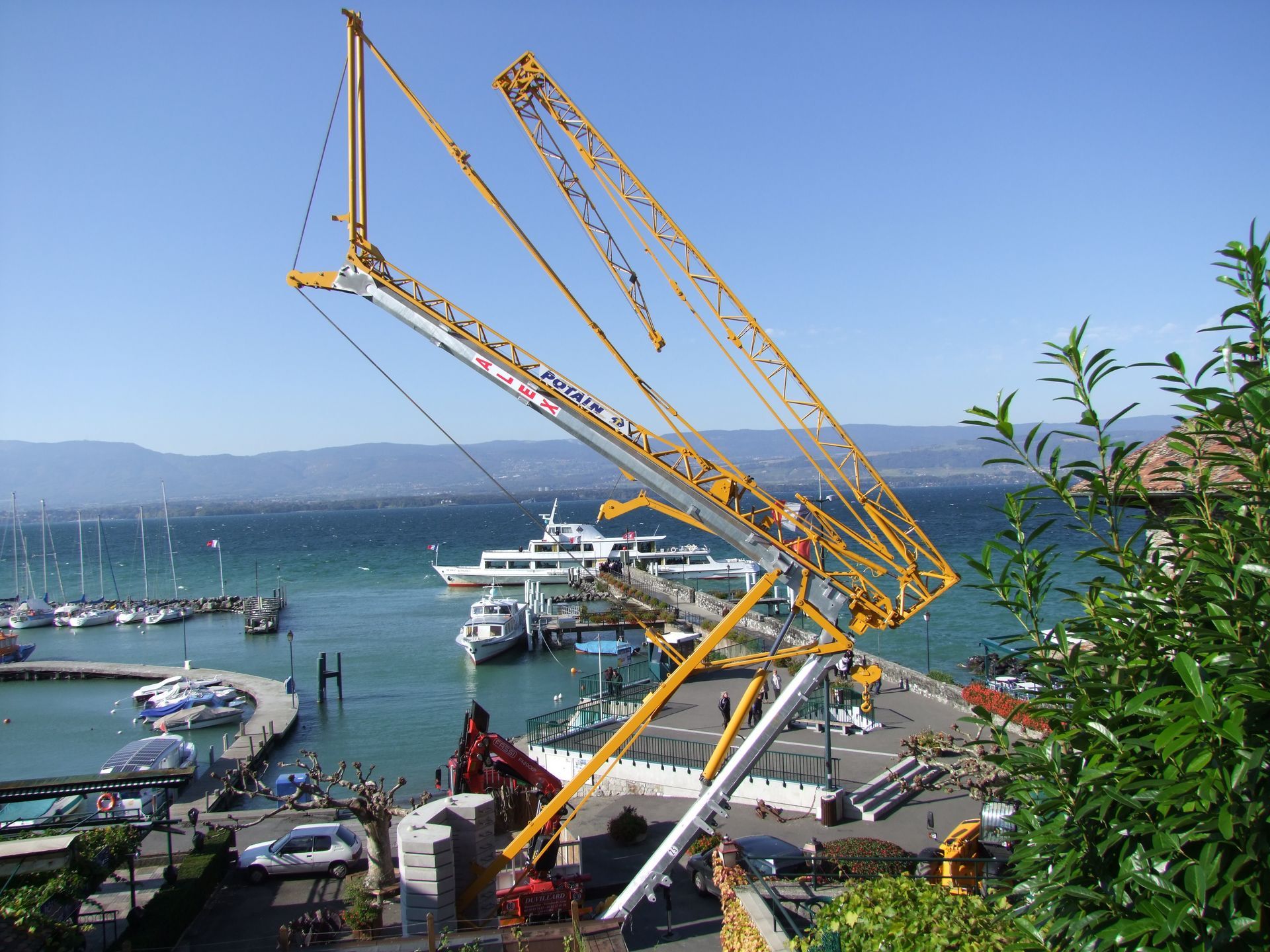 Une grue de chantier jaune, inclinée au-dessus d'une jetée, d'un port et d'un lac.