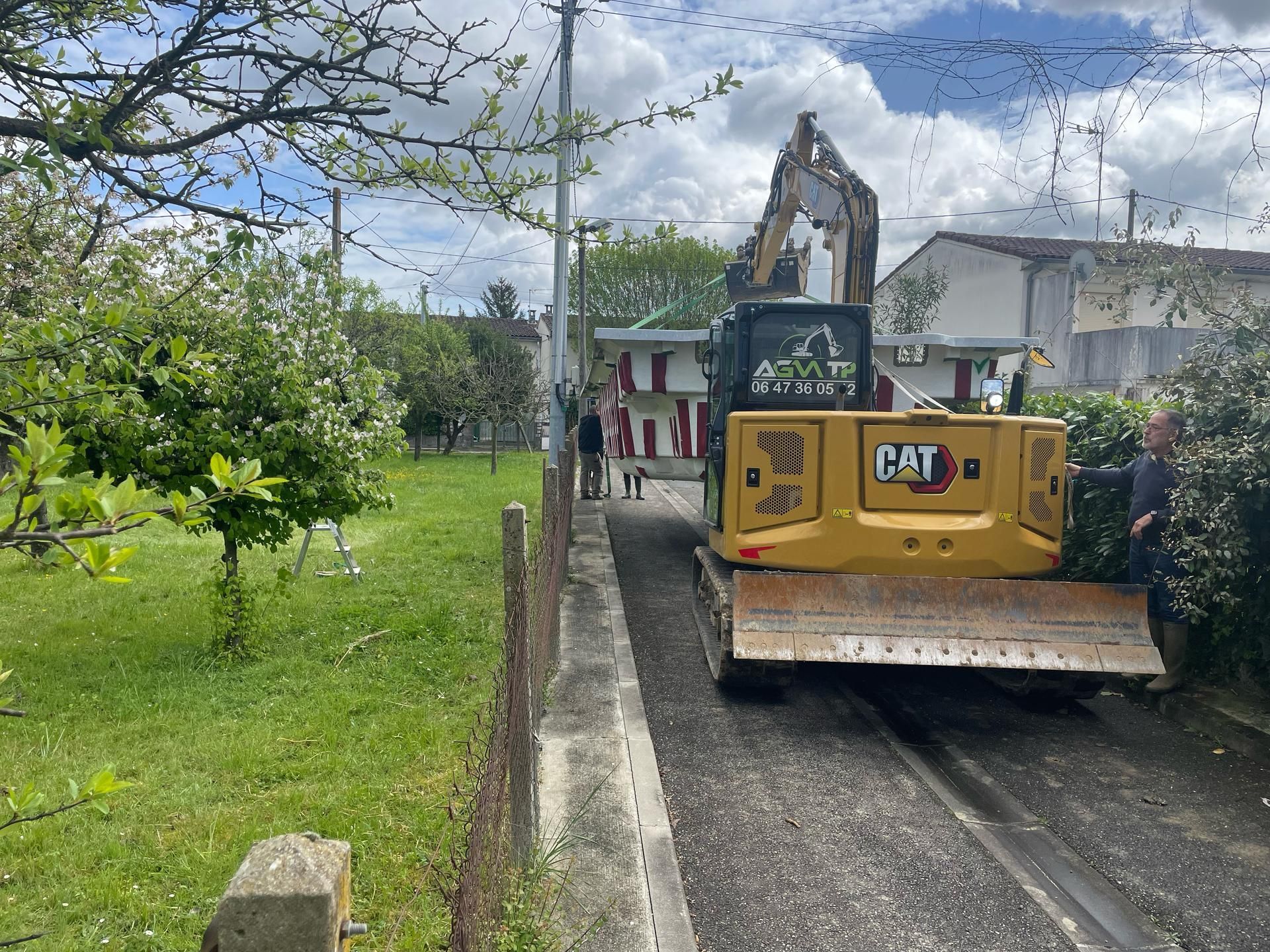Une pelleteuse CAT jaune circule sur une route goudronnée étroite.