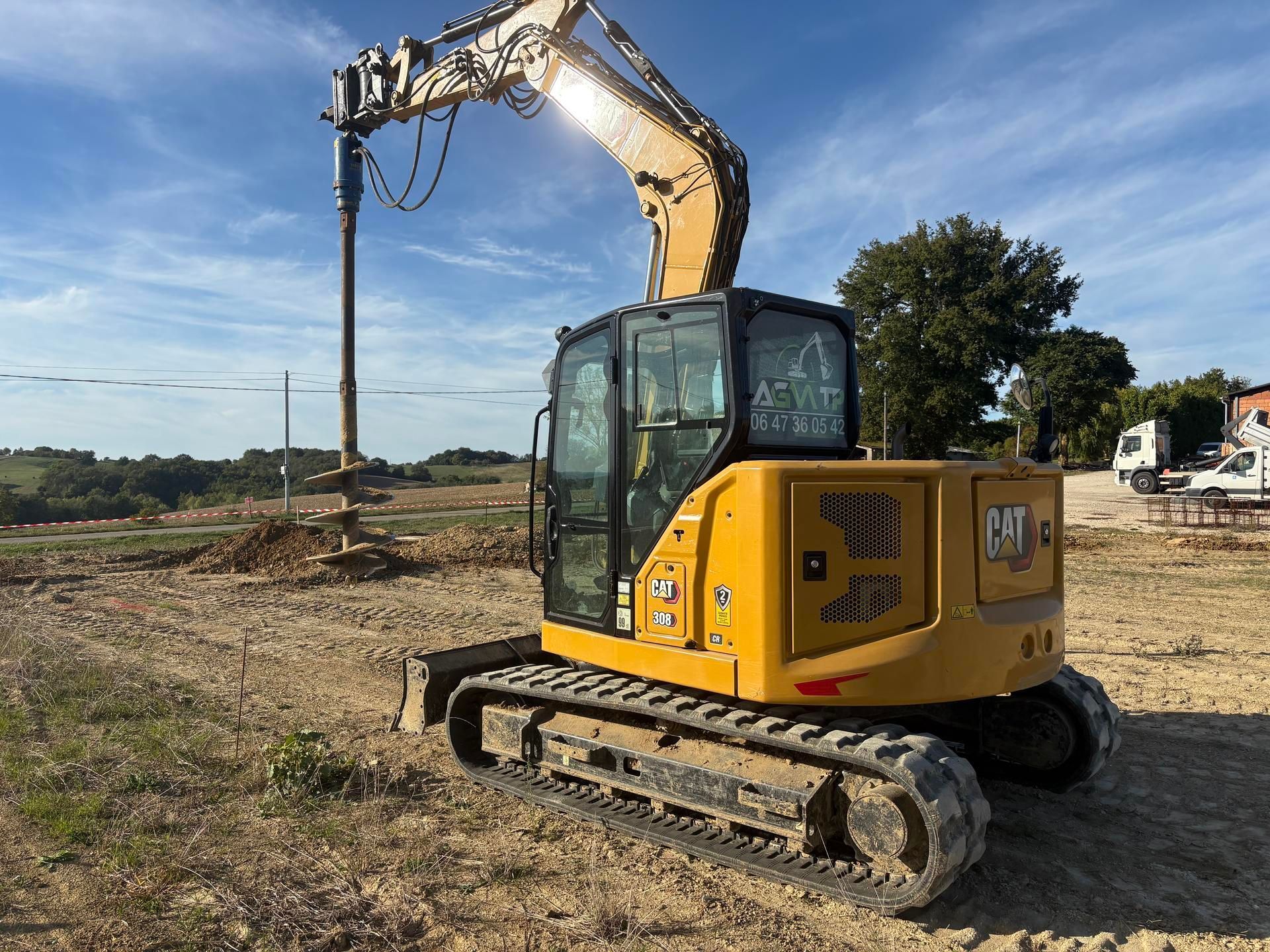 Une pelle mécanique Caterpillar jaune effectue un forage dans un champ par une journée ensoleillée.