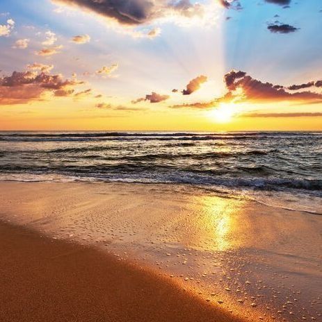 El sol se está poniendo sobre el océano y las olas rompen en la playa.