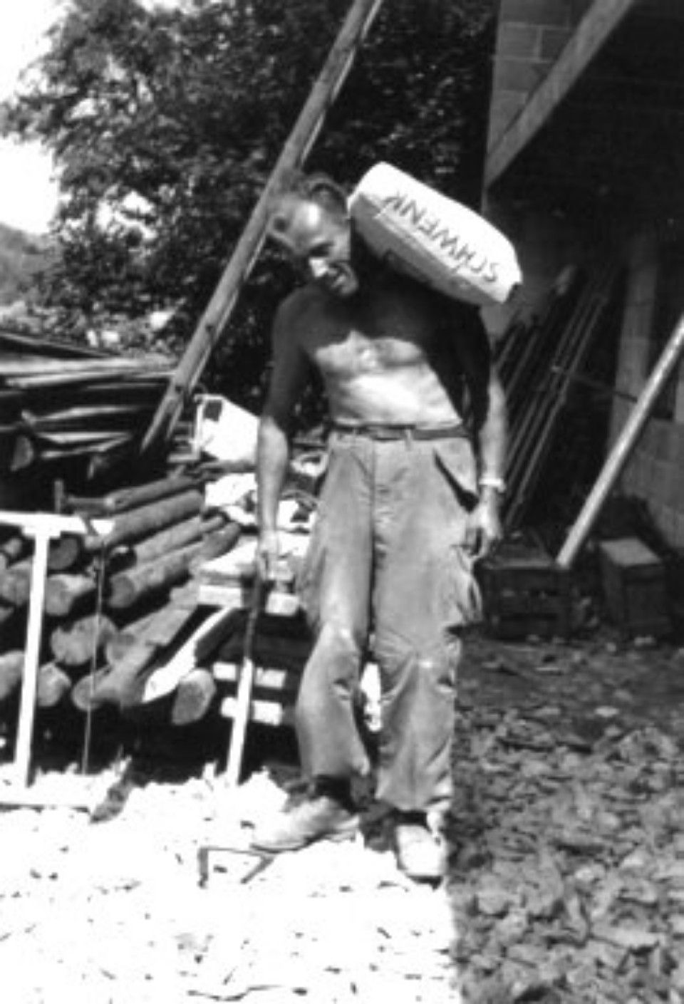 Mann mit nacktem Oberkörper trägt einen Sack Zement