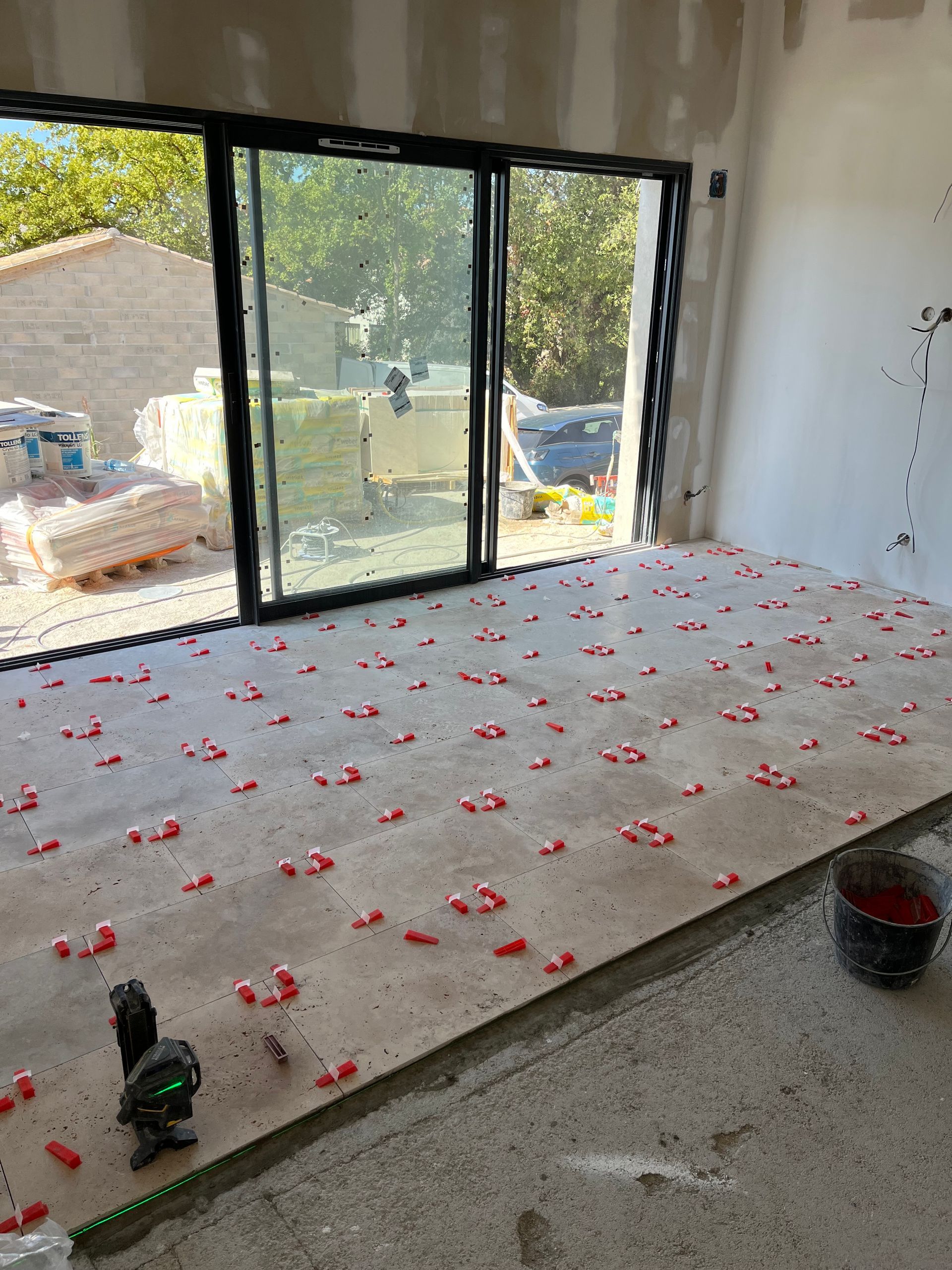 Personne posant du carrelage sur un sol en béton, appliquant le carrelage sur le mortier avec les mains.