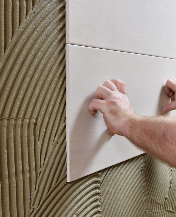 Salle de bains avec mur en carrelage hexagonal noir, miroir à cadre doré, lavabo blanc et porte de douche en verre.
