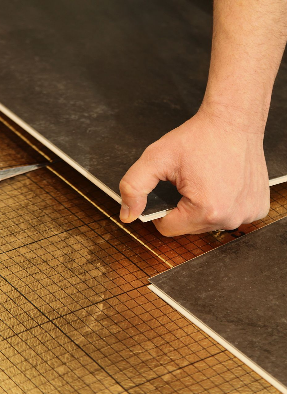 Pose manuelle de carreaux de sol gris foncé sur des carreaux installés sur du bois.