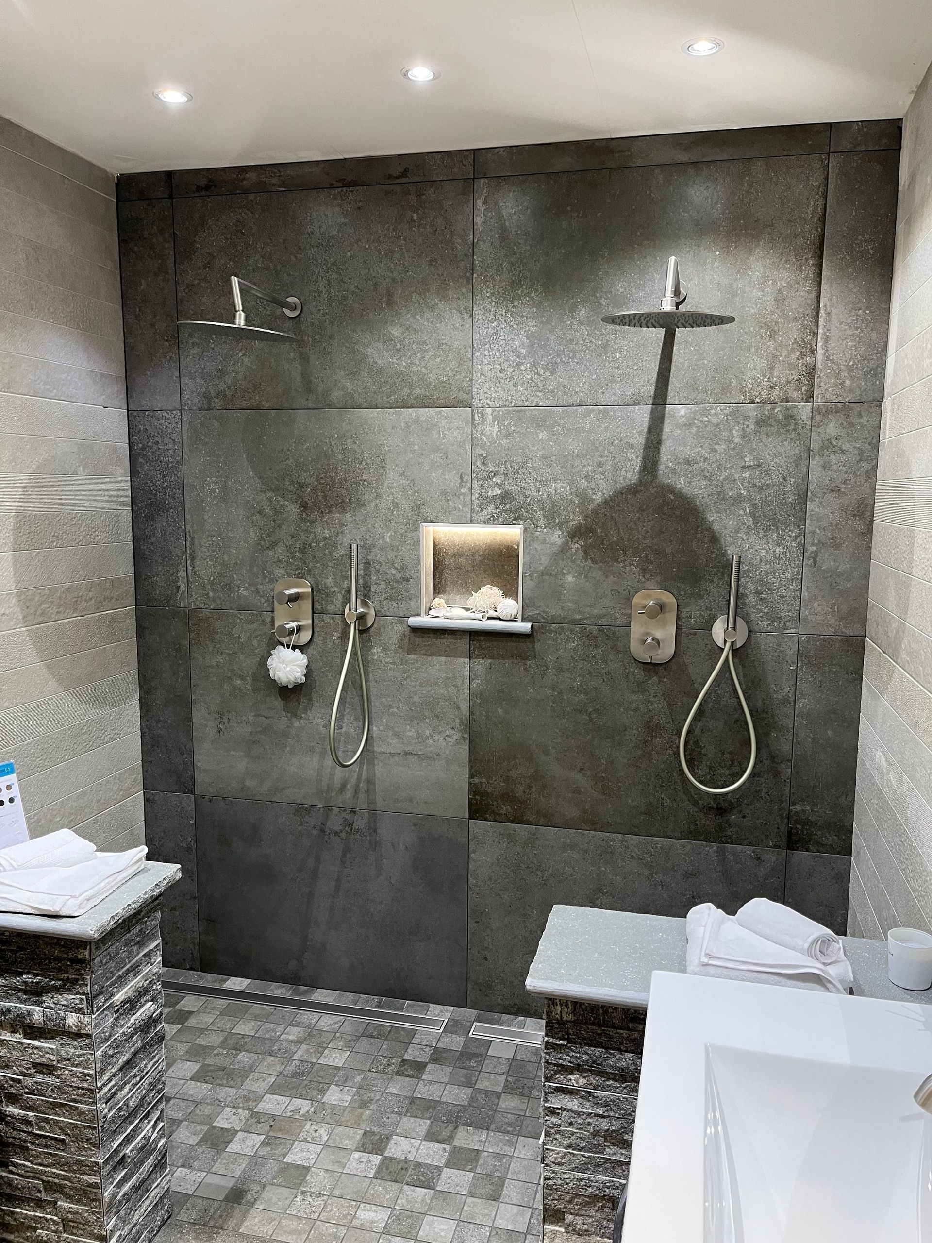 Salle de bains avec vanité flottante en bois, lavabo blanc, baignoire et sol carrelé foncé.