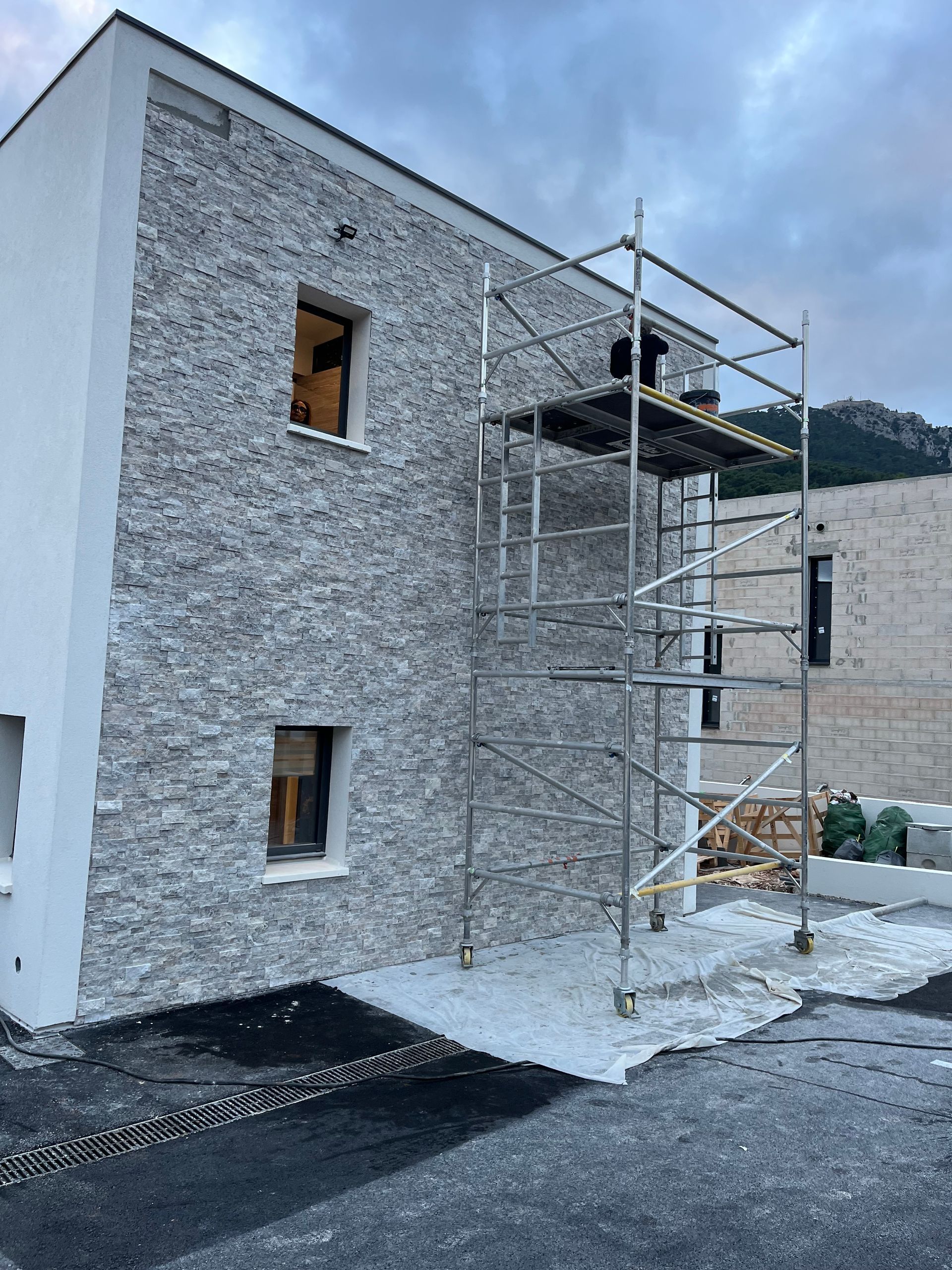 Personne posant une tuile rectangulaire grise sur un lit de mortier gris.