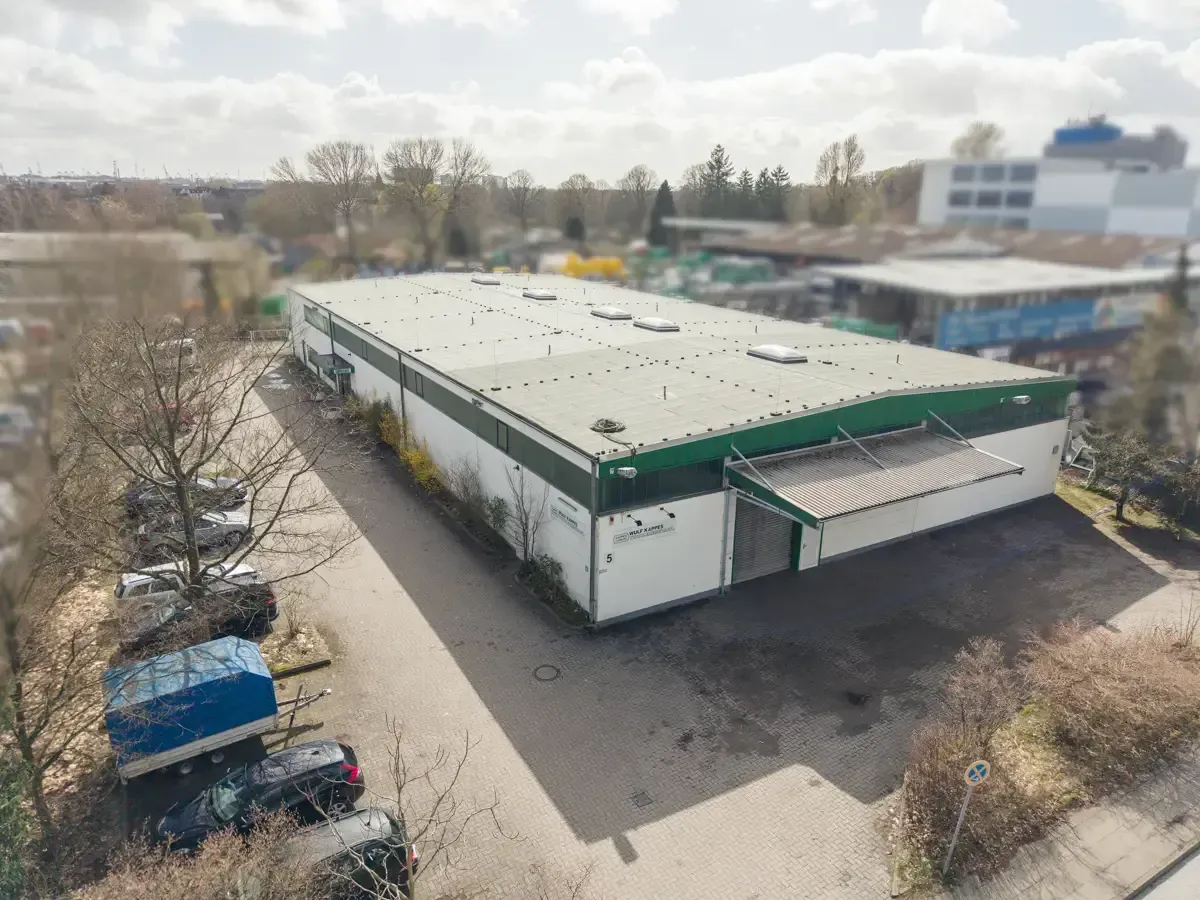 Luftaufnahme eines weißen Lagerhauses mit grünen Zierelementen neben einer Straße und geparkten Fahrzeugen
