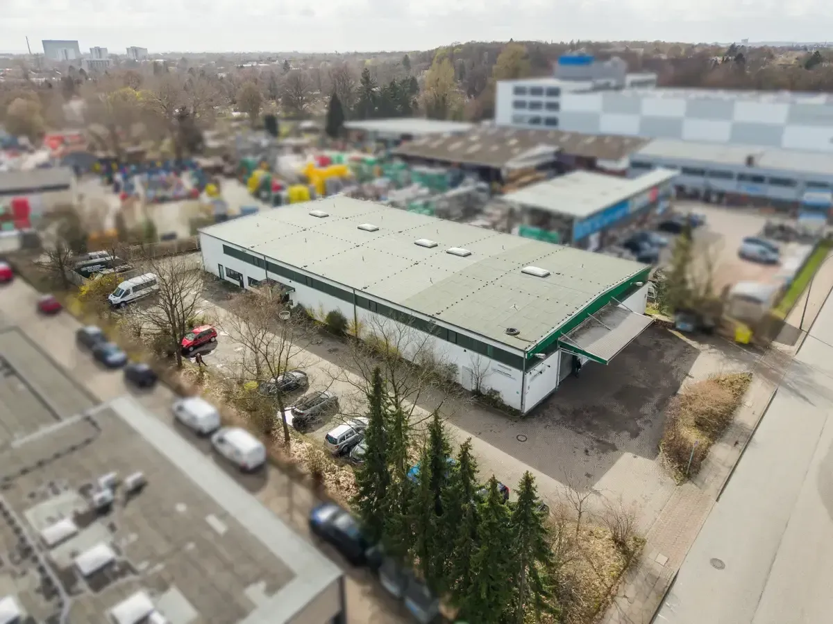 Luftaufnahme einer großen Lagerhalle mit Gründach, geparkten Autos und umliegenden Bäumen in einem Industriegebiet