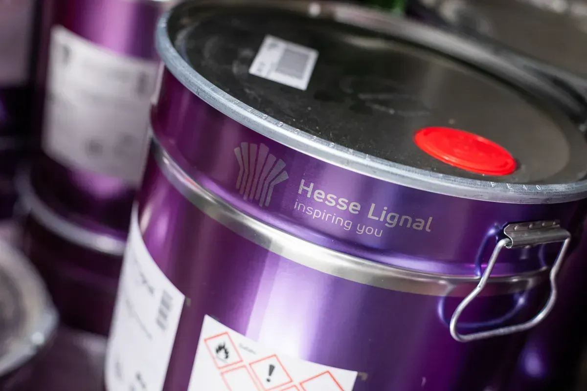Nahaufnahme eines violetten Metallbehälters mit dem Logo „Hesse Lignal“, Warnhinweisen und einem roten Deckel.