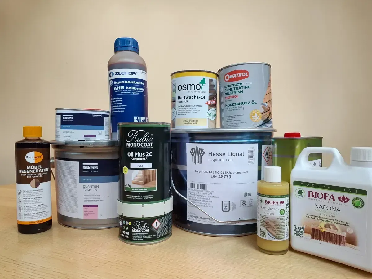 Auf einem Tisch stehen verschiedene Behälter mit Farben und Holzbeizen unterschiedlicher Größe, Form und Marke.