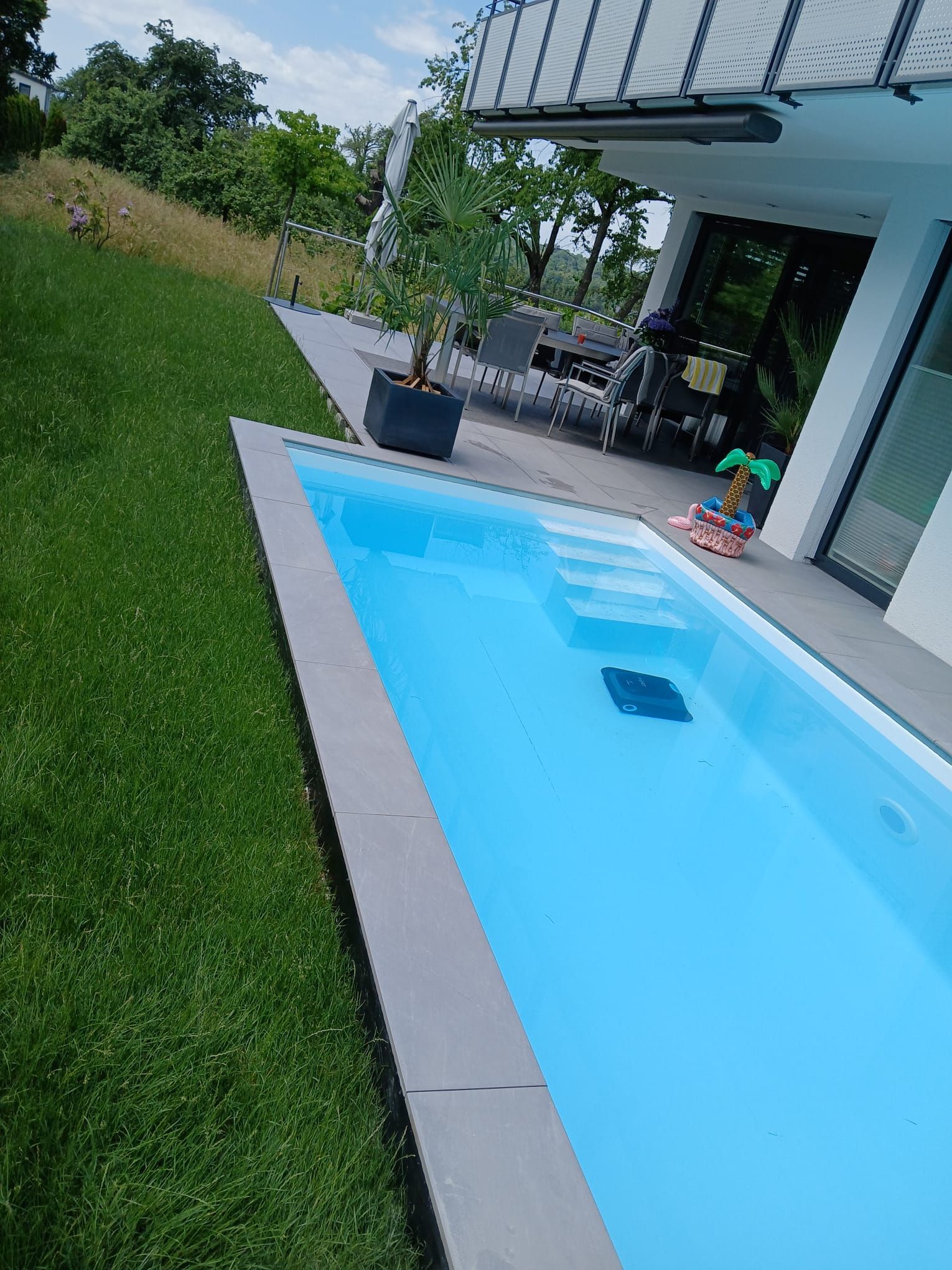 Moderne Terrasse mit kleinem blauen Pool, grünem Rasen und überdachtem Sitzbereich