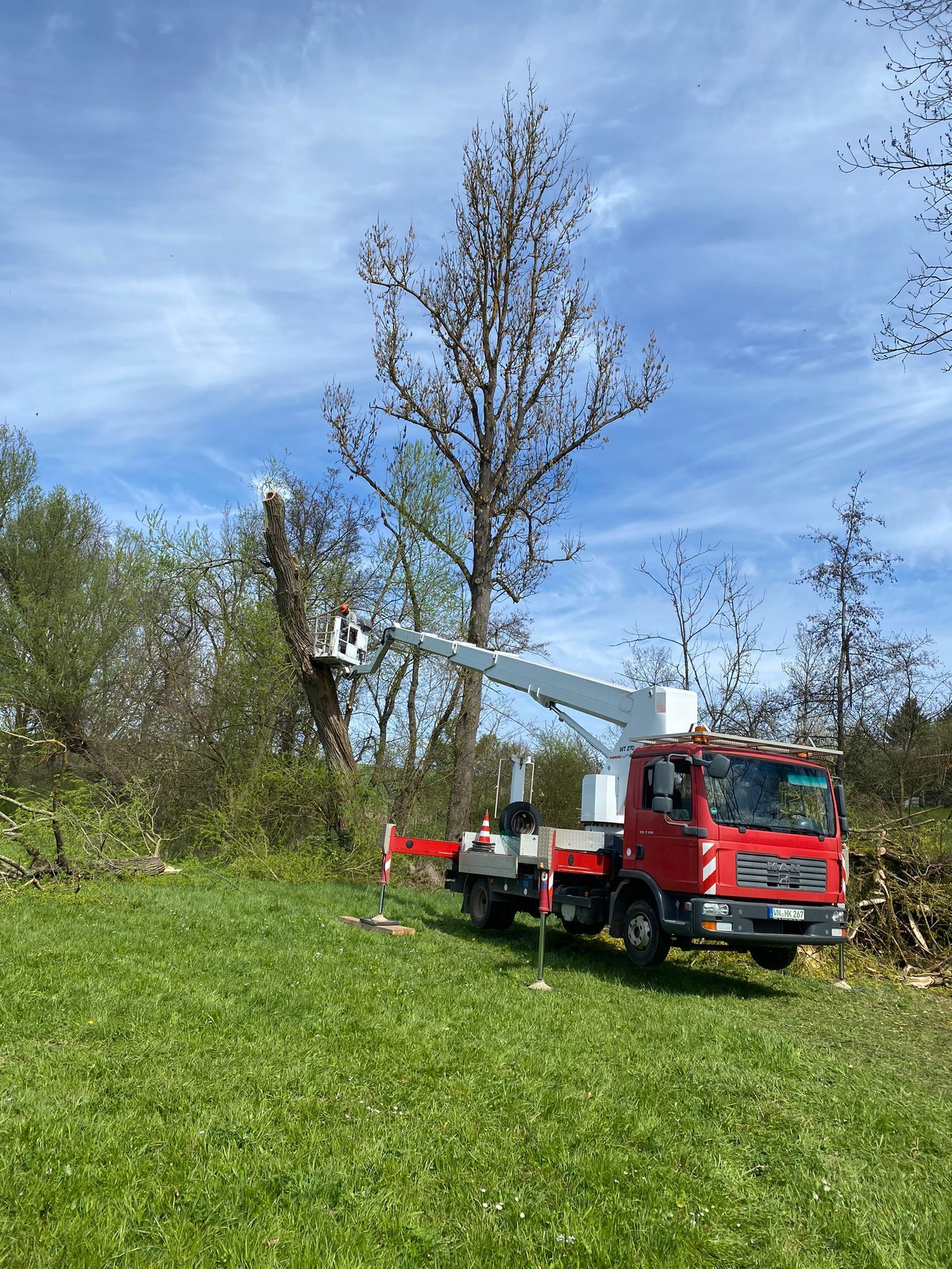Ein roter Geländewagen mit Kran steht auf einer Wiese unter blauem Himmel