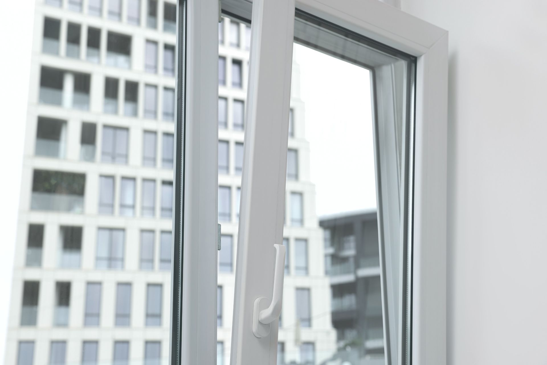 Una ventana blanca con vista a un edificio alto está abierta.