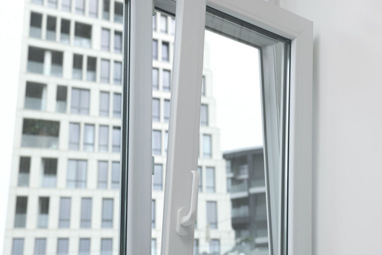 Una ventana blanca con vista a un edificio alto está abierta.
