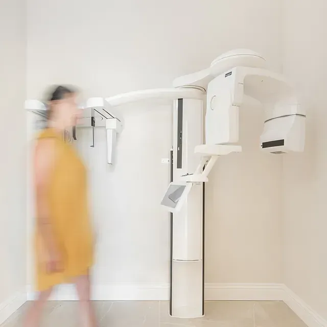 Una mujer con un vestido amarillo está parada frente a una máquina de rayos X.