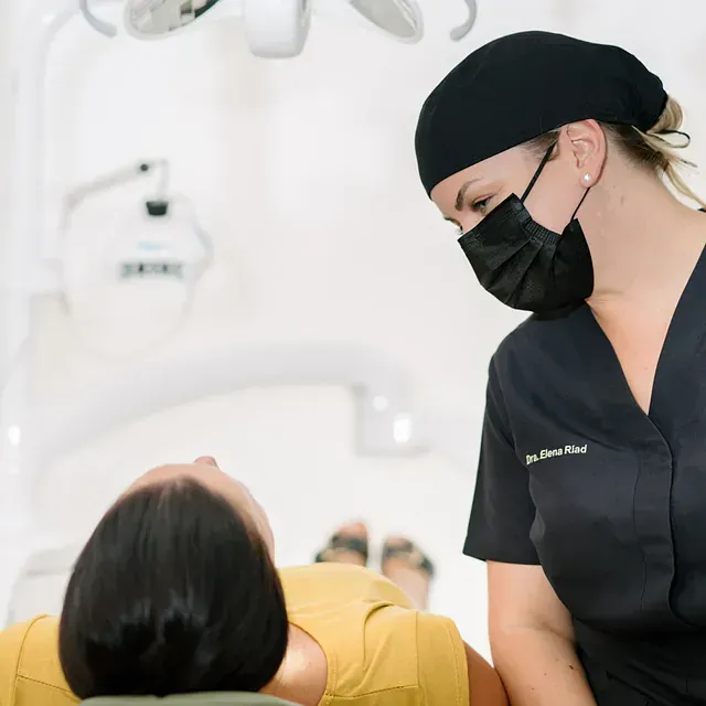 Una dentista con mascarilla habla con un paciente.