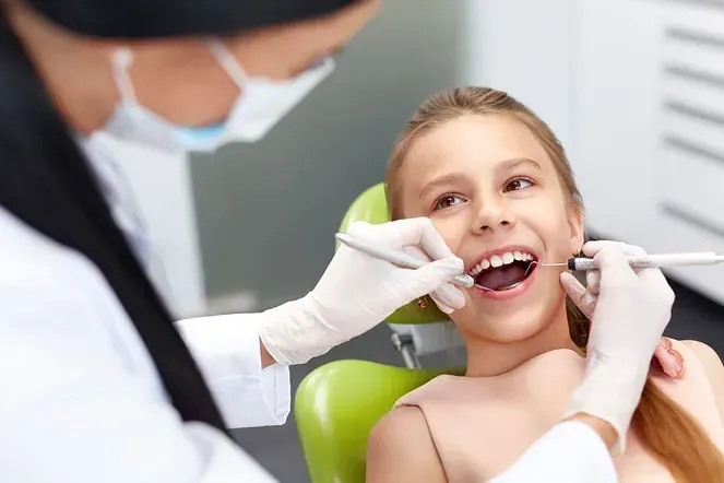 Una niña está sentada en una silla dental mientras un dentista le examina los dientes.