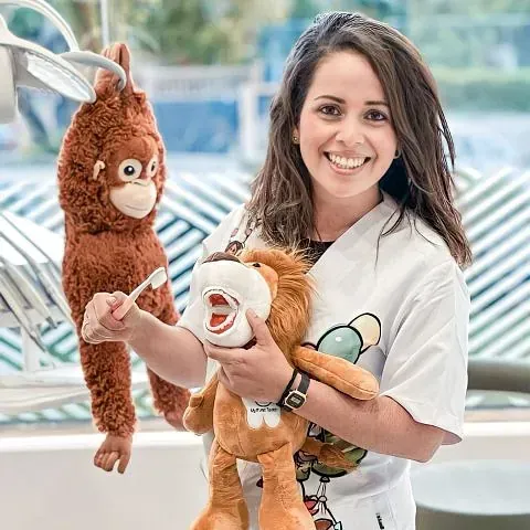 Una mujer sostiene un animal de peluche y un cepillo de dientes en un consultorio dental.