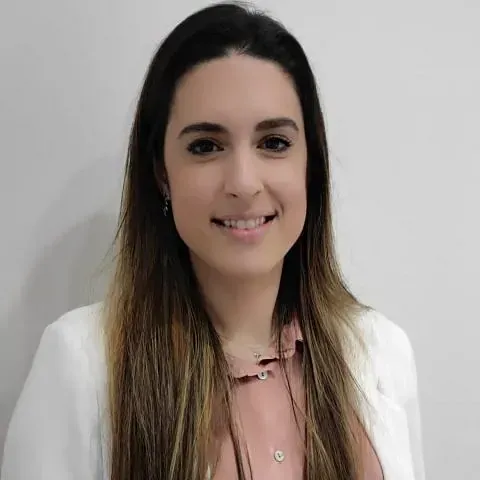 Una mujer que lleva una chaqueta blanca y una camisa rosa sonríe a la cámara.