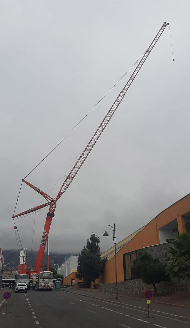 Gran grúa naranja en un día nublado, instalada a lo largo de una carretera al lado de un edificio.
