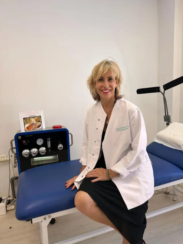 Profesional médico con bata blanca sentado en una camilla de exploración en una sala de consulta.
